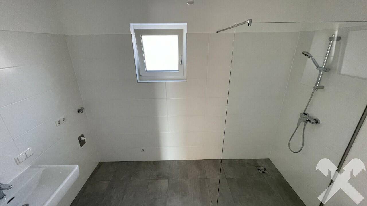 Modernes Badezimmer mit begehbarer Dusche, Dachfenster und Waschbecken in hellem Design.