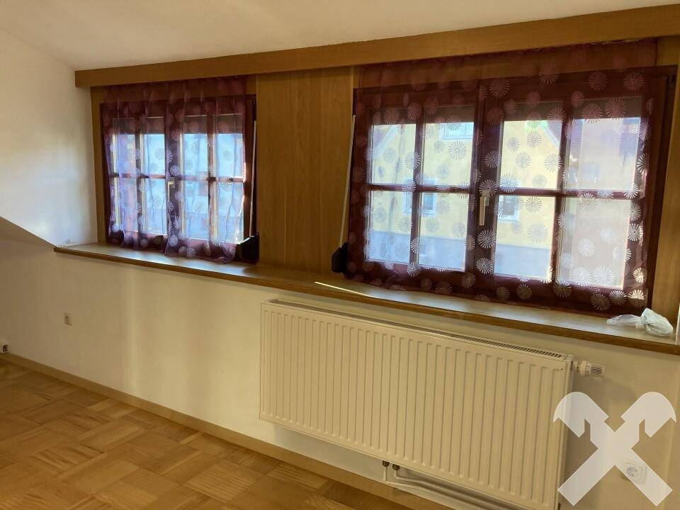 Gemütlicher Raum mit zwei Fenstern, Holzverkleidung und Heizkörper, ideal als Schlafzimmer.