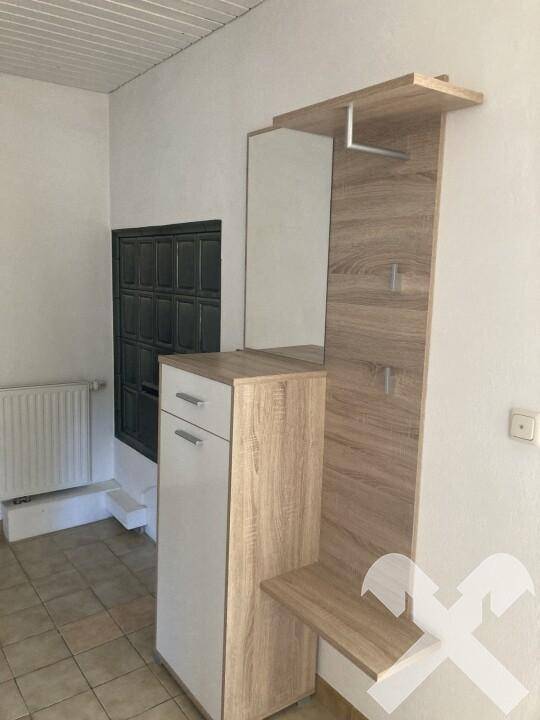 Eingangsbereich mit moderner Garderobe, Fliesenboden und sichtbarem Kachelofen im Hintergrund.