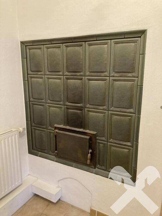 Detailaufnahme eines traditionellen grünen Kachelofens mit Metalltür, ein Heizelement des Raumes.