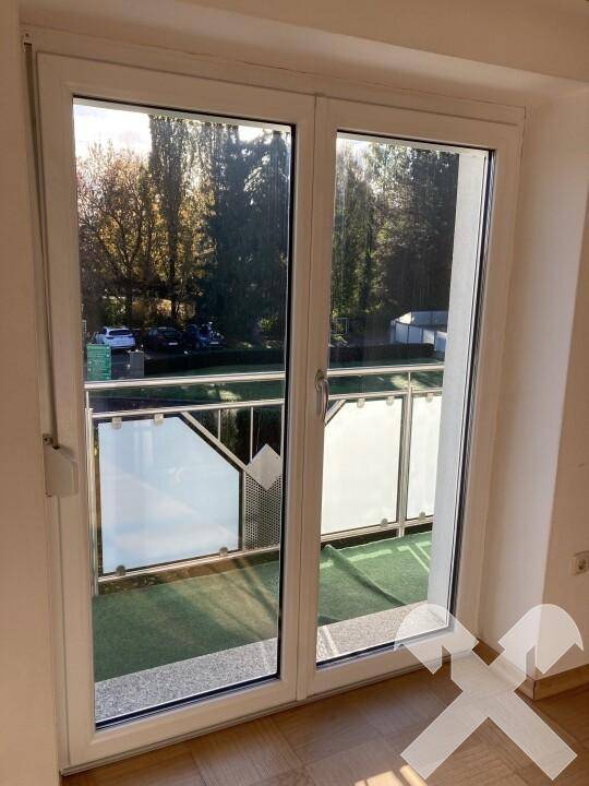 Große Balkontür mit Zugang zu einem kleinen Balkon, der einen grünen Ausblick bietet.