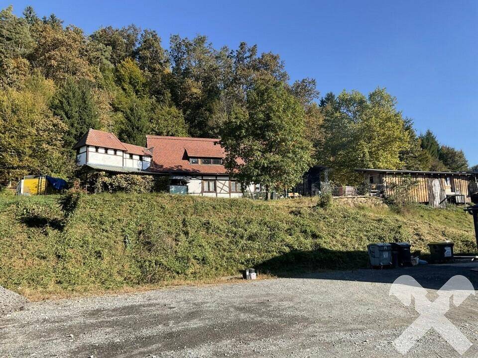 Gesamtansicht des Anwesens mit mehreren Gebäuden am bewaldeten Hang unter blauem Himmel.