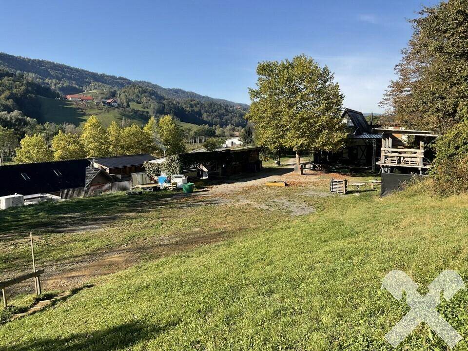 Weitläufiges Gelände mit Grasflächen, Bäumen und Gebäuden, umgeben von hügeliger Landschaft.