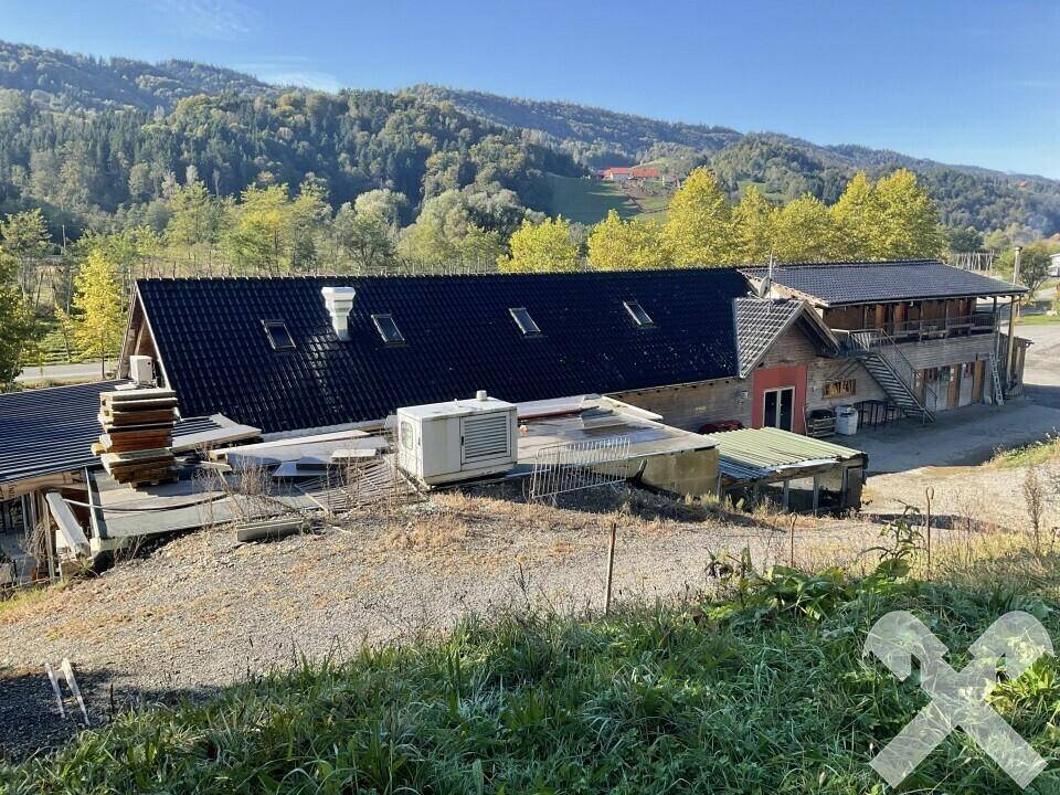 Überblick über das Anwesen mit mehreren Gebäuden und Dächern, umgeben von bewaldeten Hügeln.