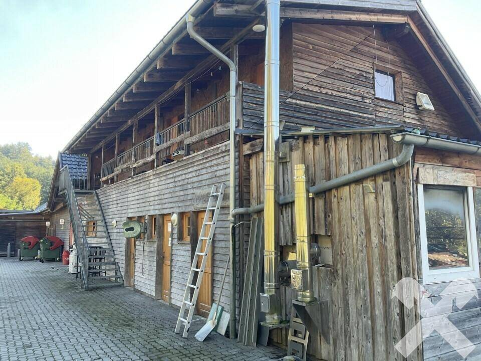 Ländliches Holzgebäude mit Außentreppe, Balkon und Metallschornsteinen unter klarem Himmel.