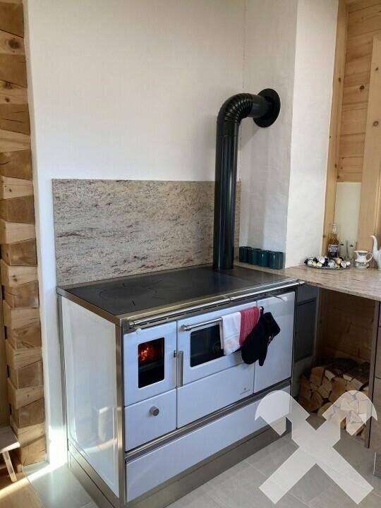 Traditioneller Holzofen mit Kochfeld und Backfunktion, umgeben von Holz und Fliesen.