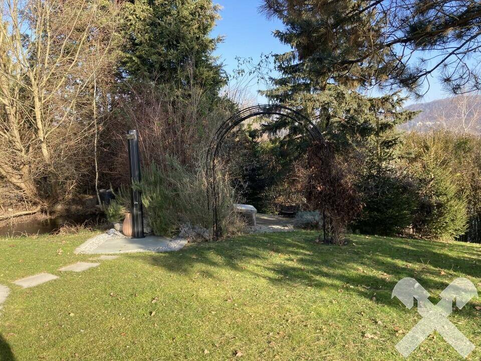 Idyllischer Gartenbereich mit Teich, grüner Wiese und einem dekorativen Metallbogen.
