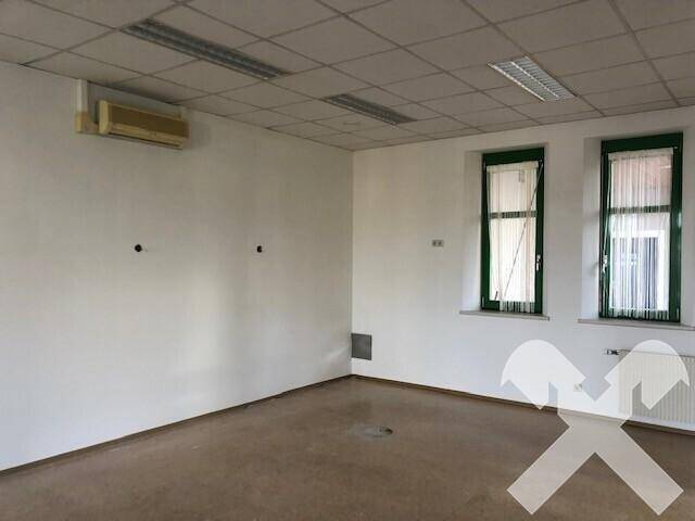 Büroraum mit weißen Wänden, abgehängter Decke, Klimaanlage und zwei Fenstern mit Vorhängen.