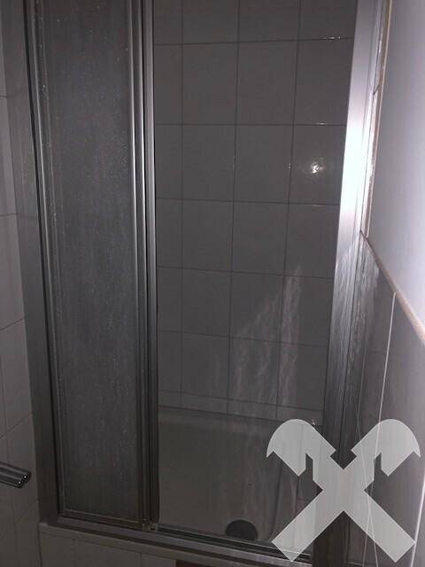 Duschkabine mit grauen Fliesen an den Wänden und einer Glastür in einem Badezimmer.