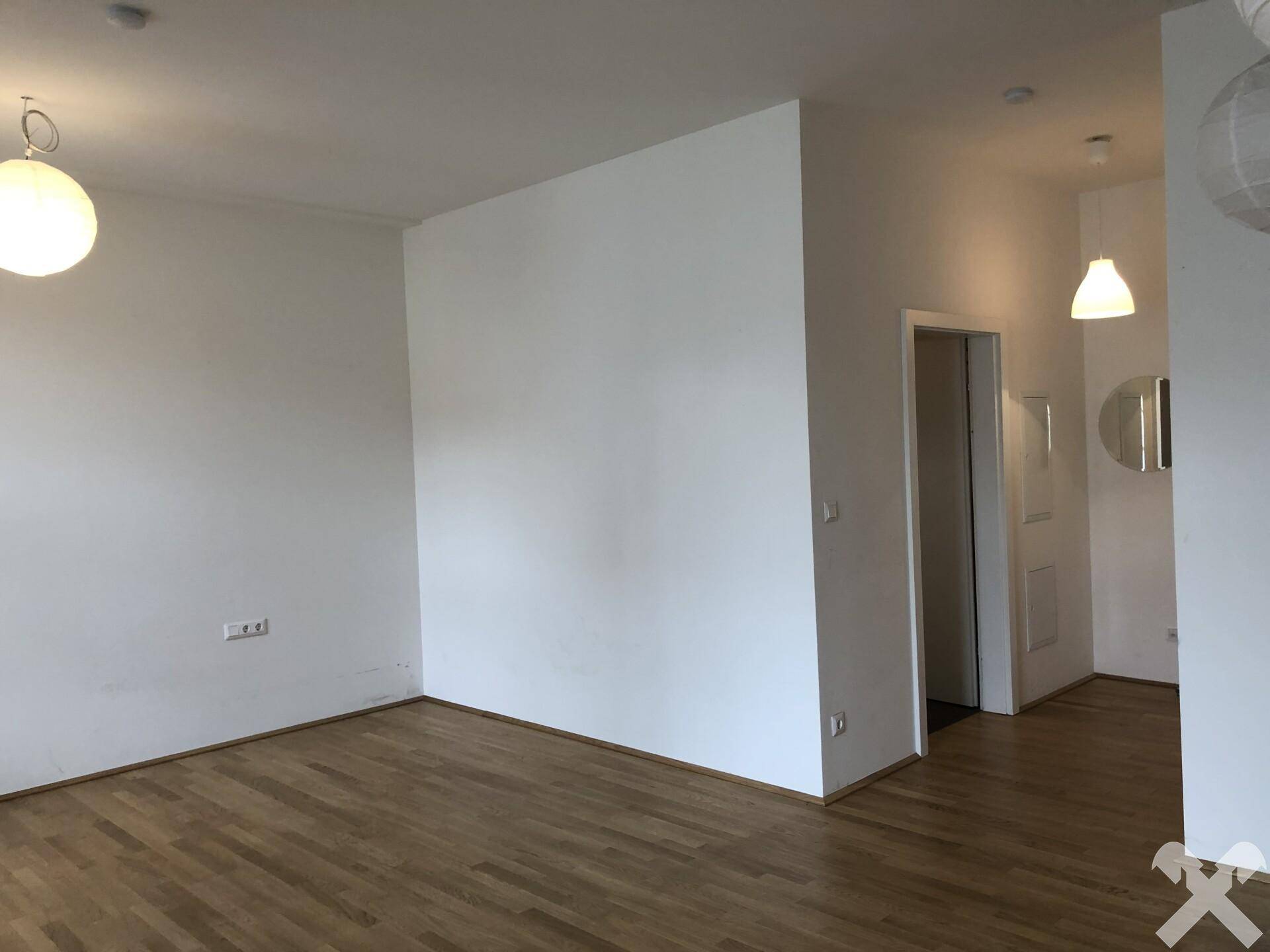 Geräumiger Wohnbereich mit hellem Holzboden und weißen Wänden, bietet Zugang zu weiteren Räumen.