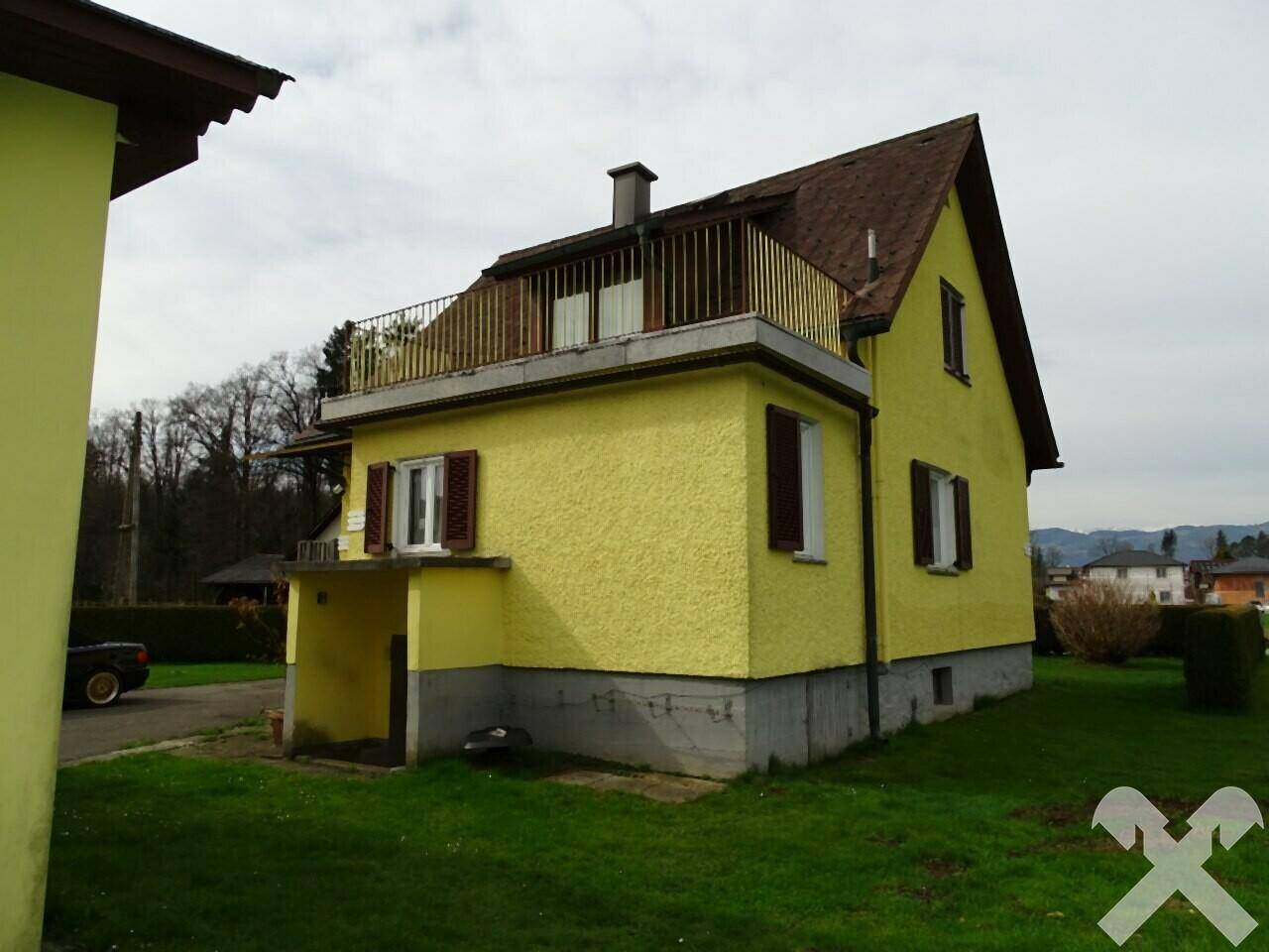 Rückansicht des gelben Hauses mit Balkon im Obergeschoss und grünem Rasen.