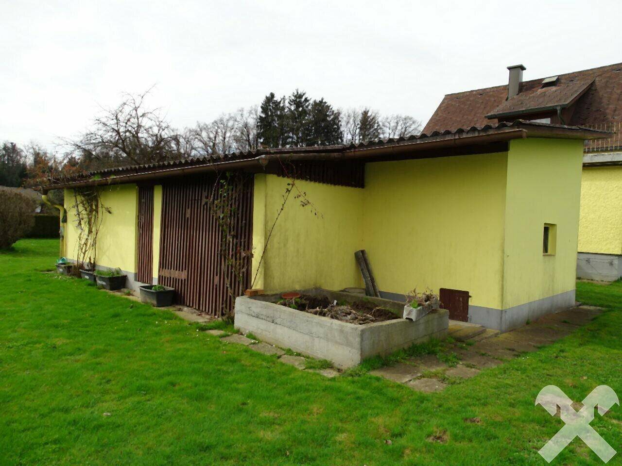 Nebengebäude mit Holztüren und einem kleinen Hochbeet im Gartenbereich.