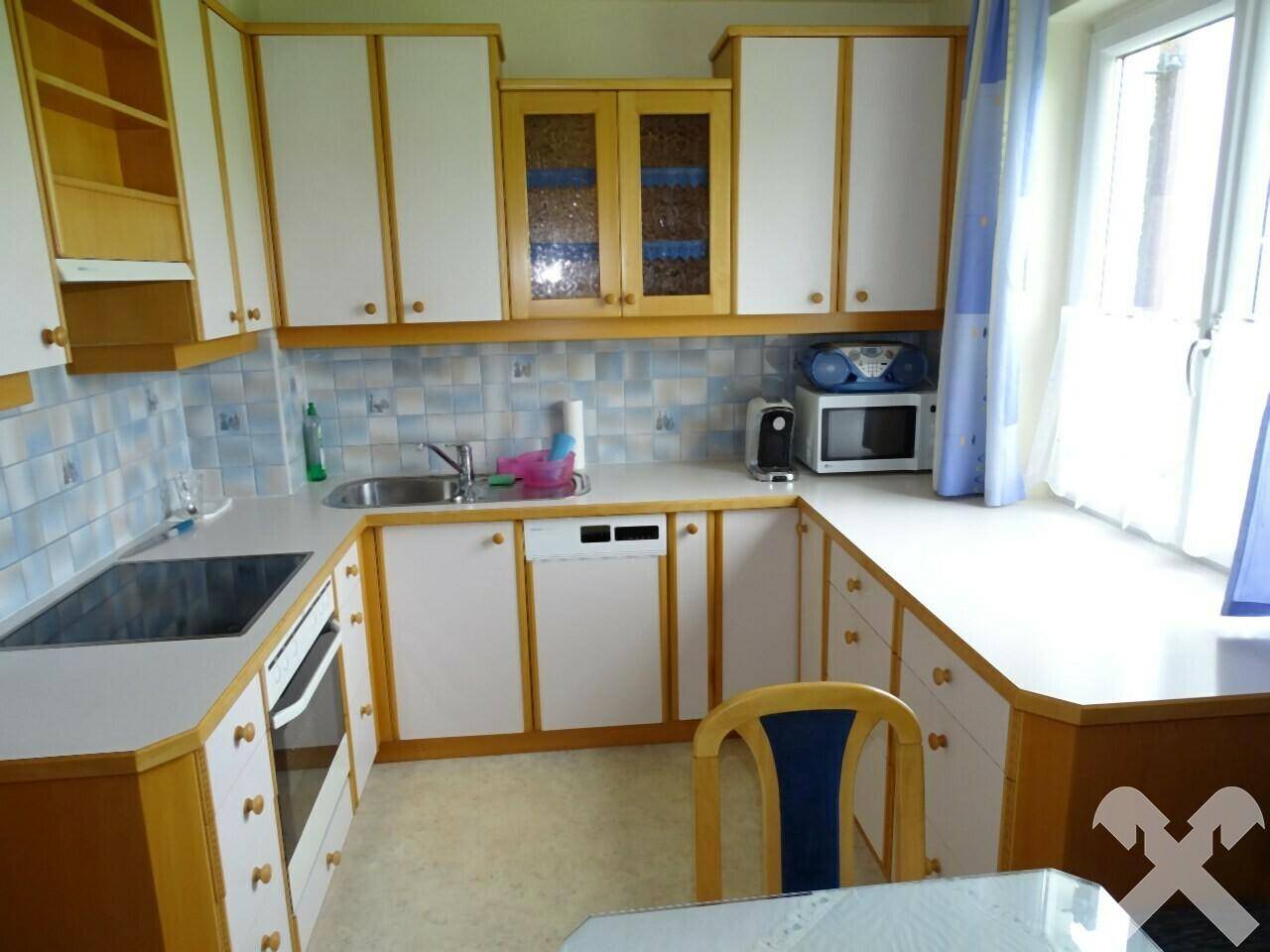 Funktionale Küche mit weißen und holzfarbenen Schränken, blauen Fliesen und Fenster.