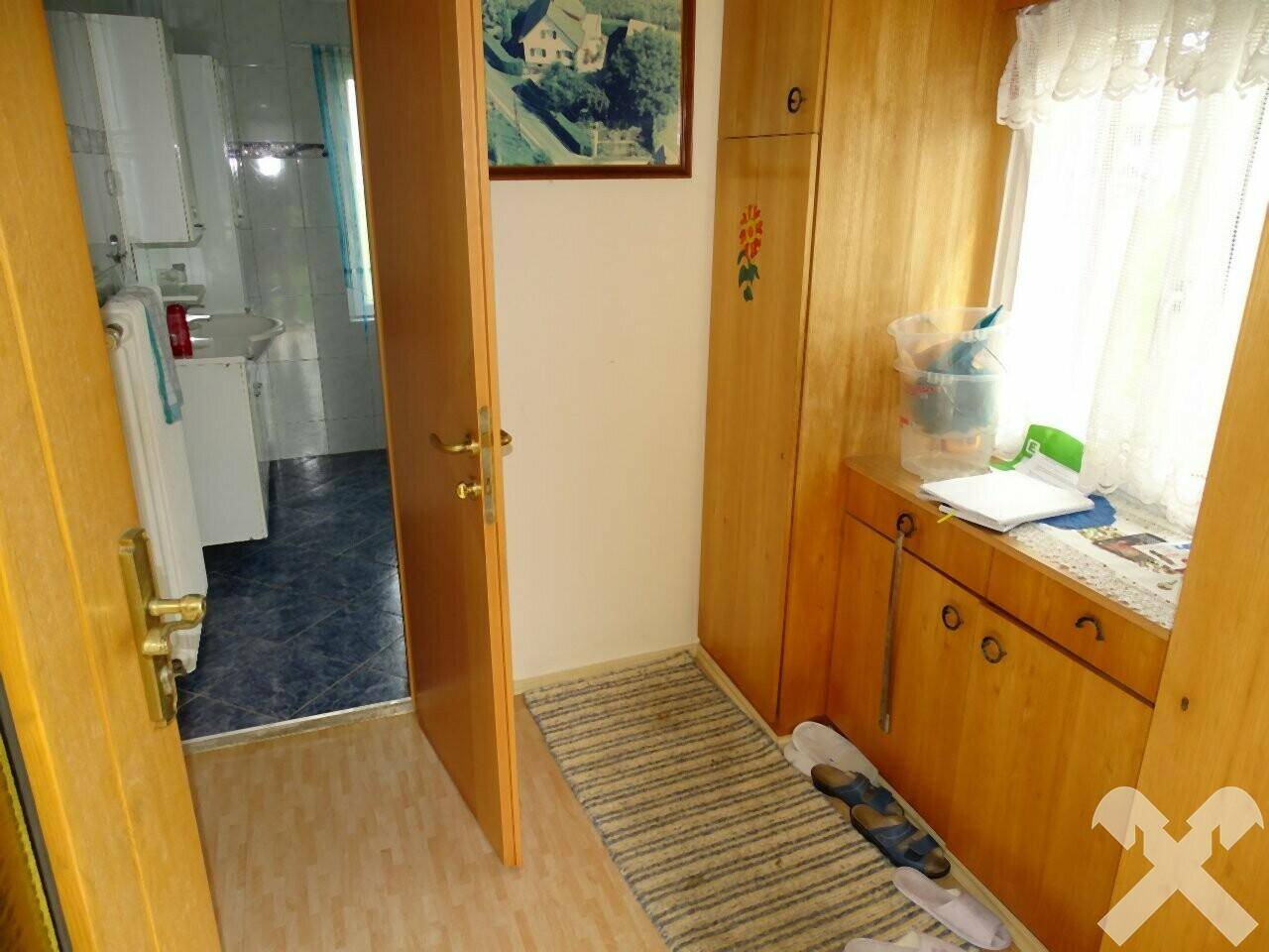 Flur mit Holzschränken und Blick in ein Badezimmer mit blauen Bodenfliesen.