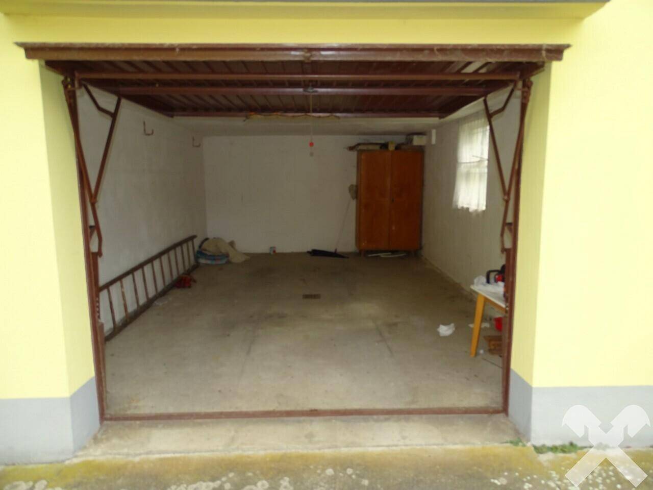 Leere Garage mit Betonboden, Leiter und einem Schrank im Hintergrund.