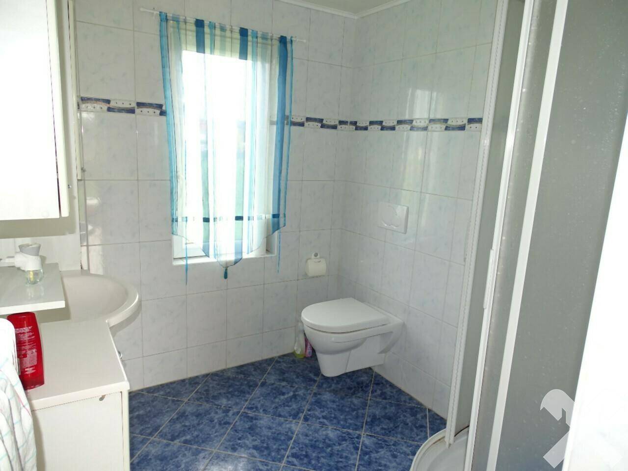 Badezimmer mit weißen und blauen Fliesen, Toilette, Waschbecken und Duschkabine.