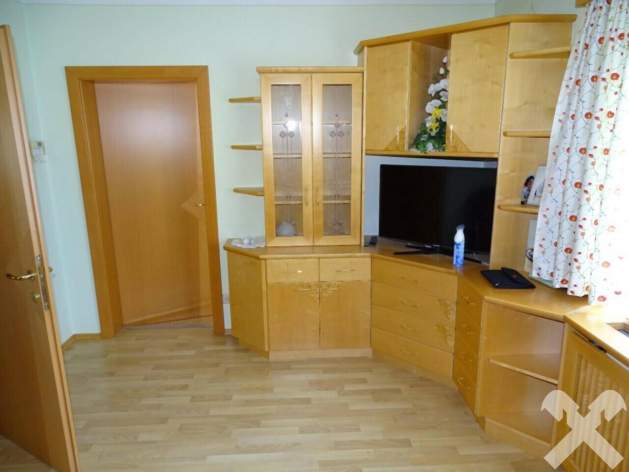 Wohnbereich mit holzfarbenen Möbeln, Fernseher und hellem Laminatboden.
