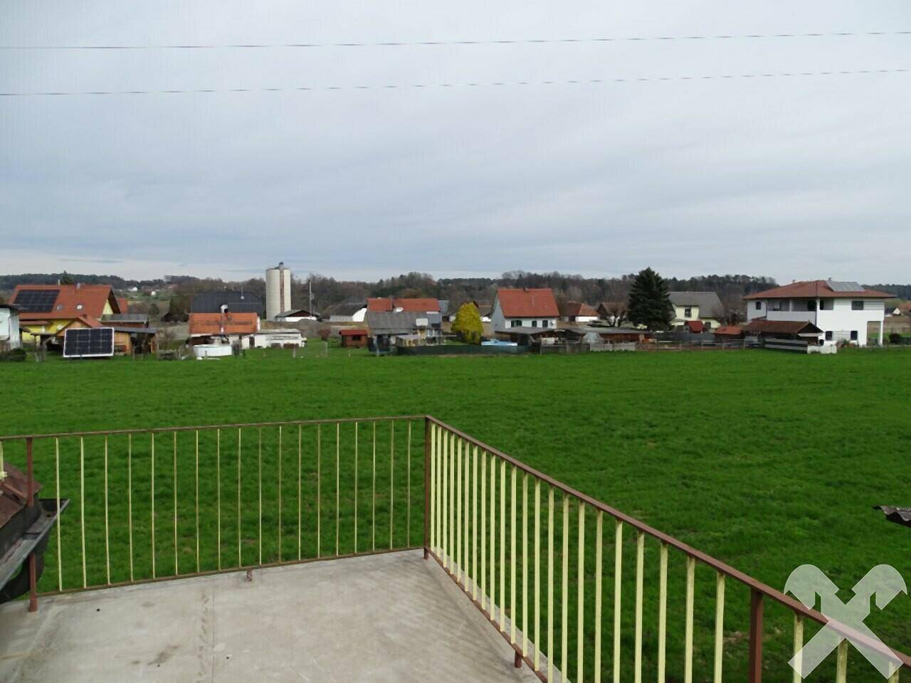Weitblick von einem Balkon über ein grünes Feld und ein Dorf in der Ferne.
