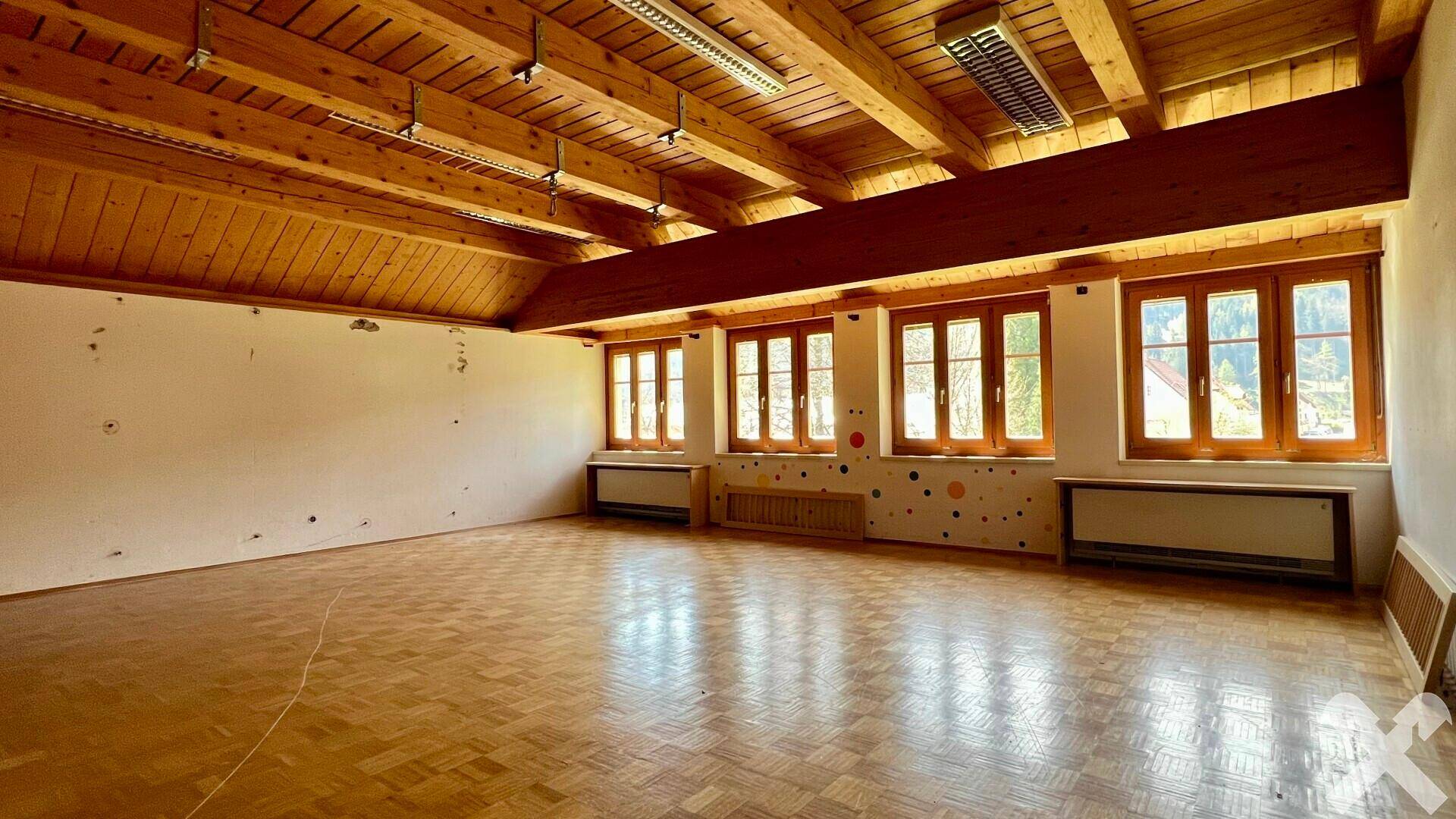 Geräumiger Innenraum mit Holzbalkendecke, Parkettboden und großen Fenstern, ideal für verschiedene Nutzungen.