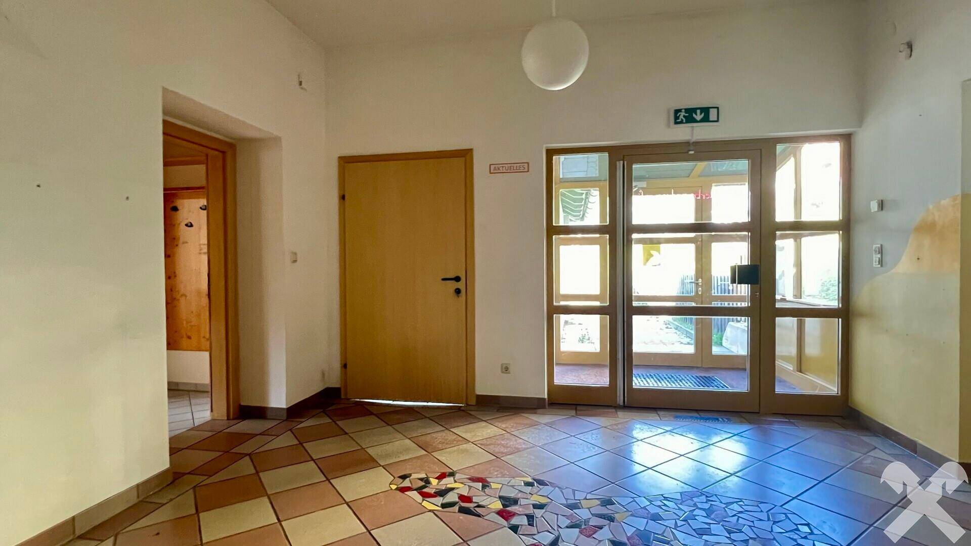 Heller Eingangsbereich mit farbenfrohem Fliesenboden, Holztüren und Glastüren, die nach draußen führen.