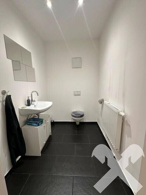 Modernes Gäste-WC mit dunklen Fliesen, wandhängendem WC und kleinem Waschbecken.
