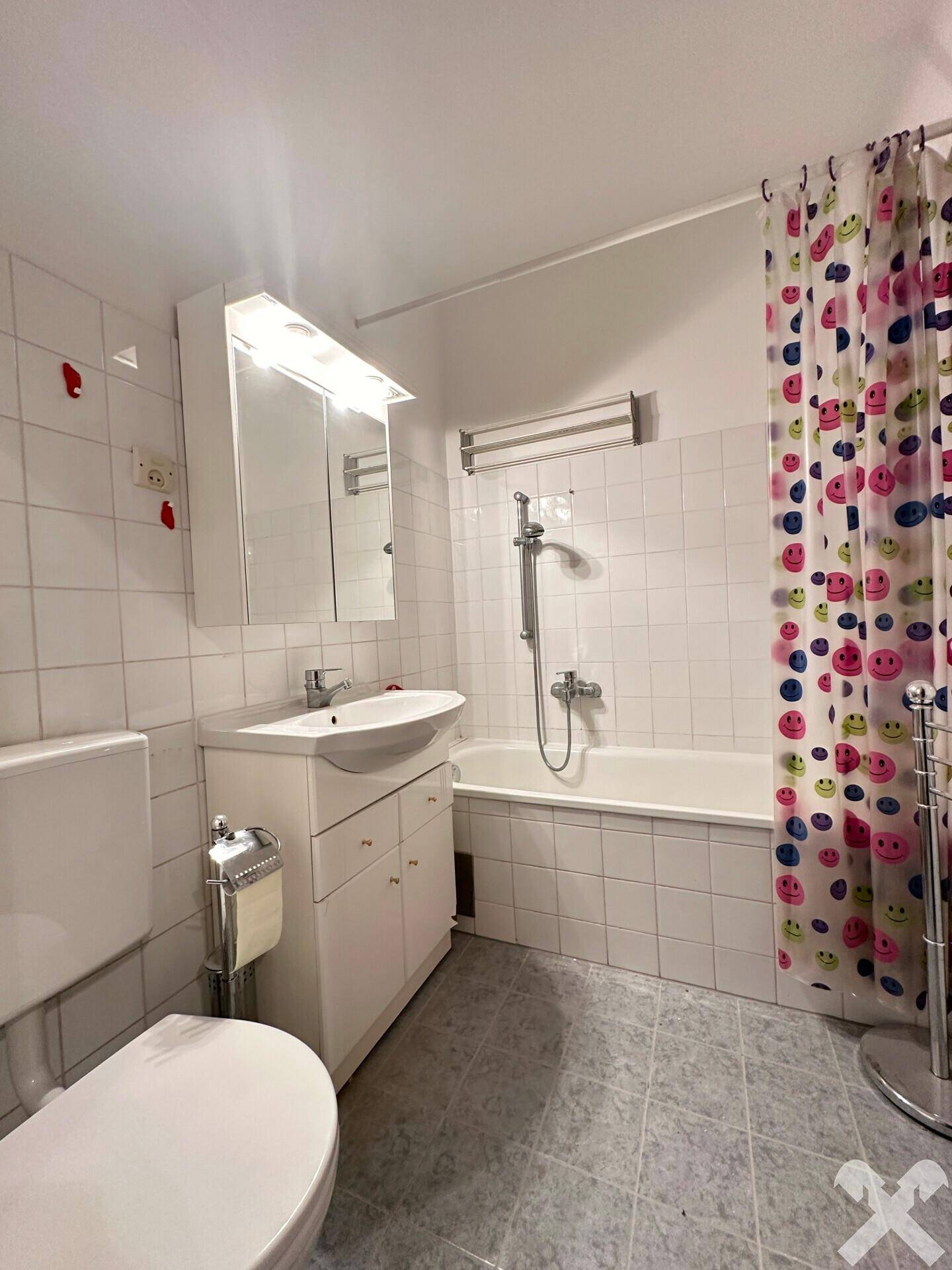 Helles Badezimmer mit Badewanne, Duschvorhang, WC und Waschbecken mit Unterschrank.