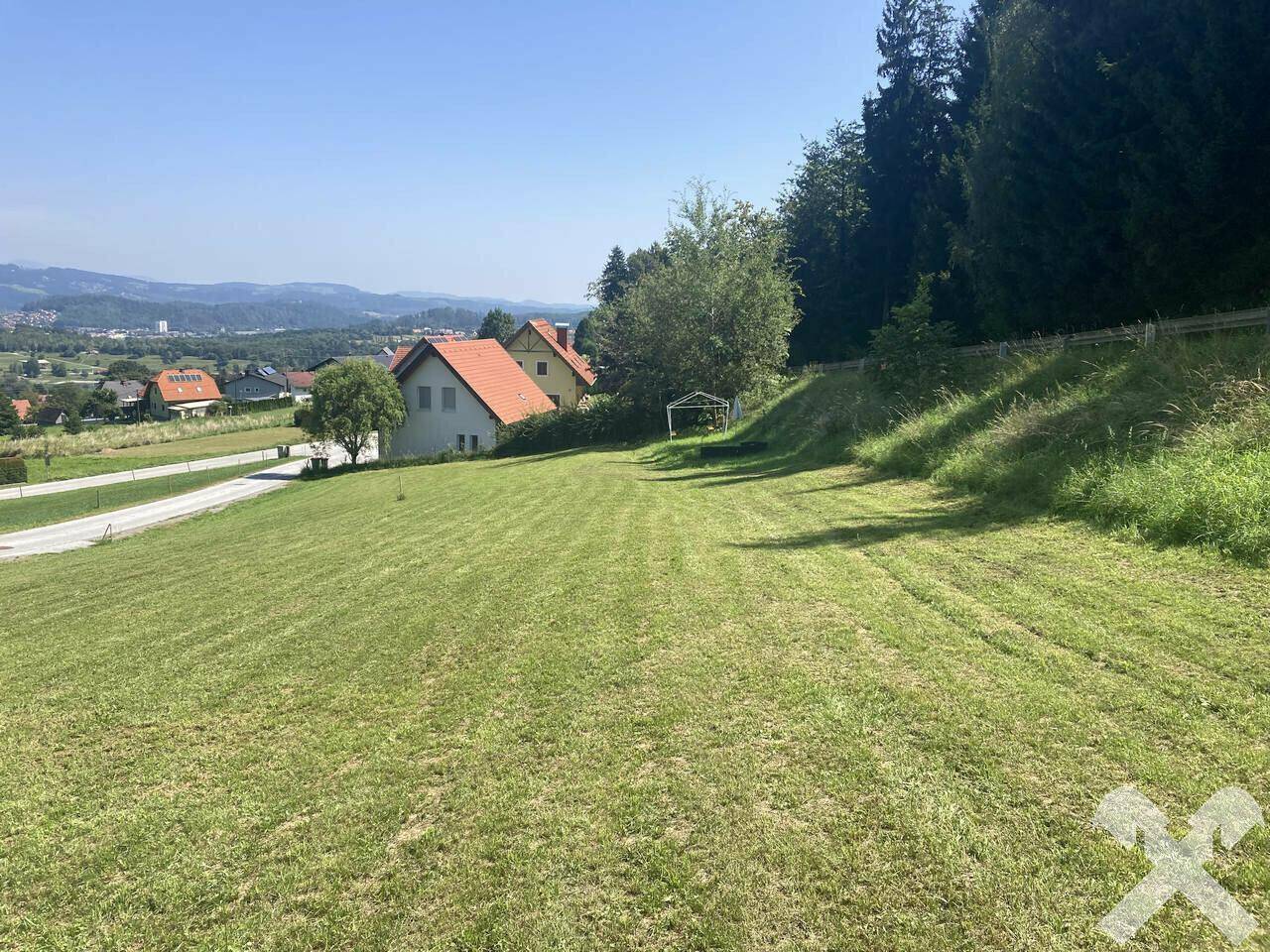 Weitläufige grüne Landschaft mit Blick auf umliegende Häuser und sanfte Hügel in der Ferne.