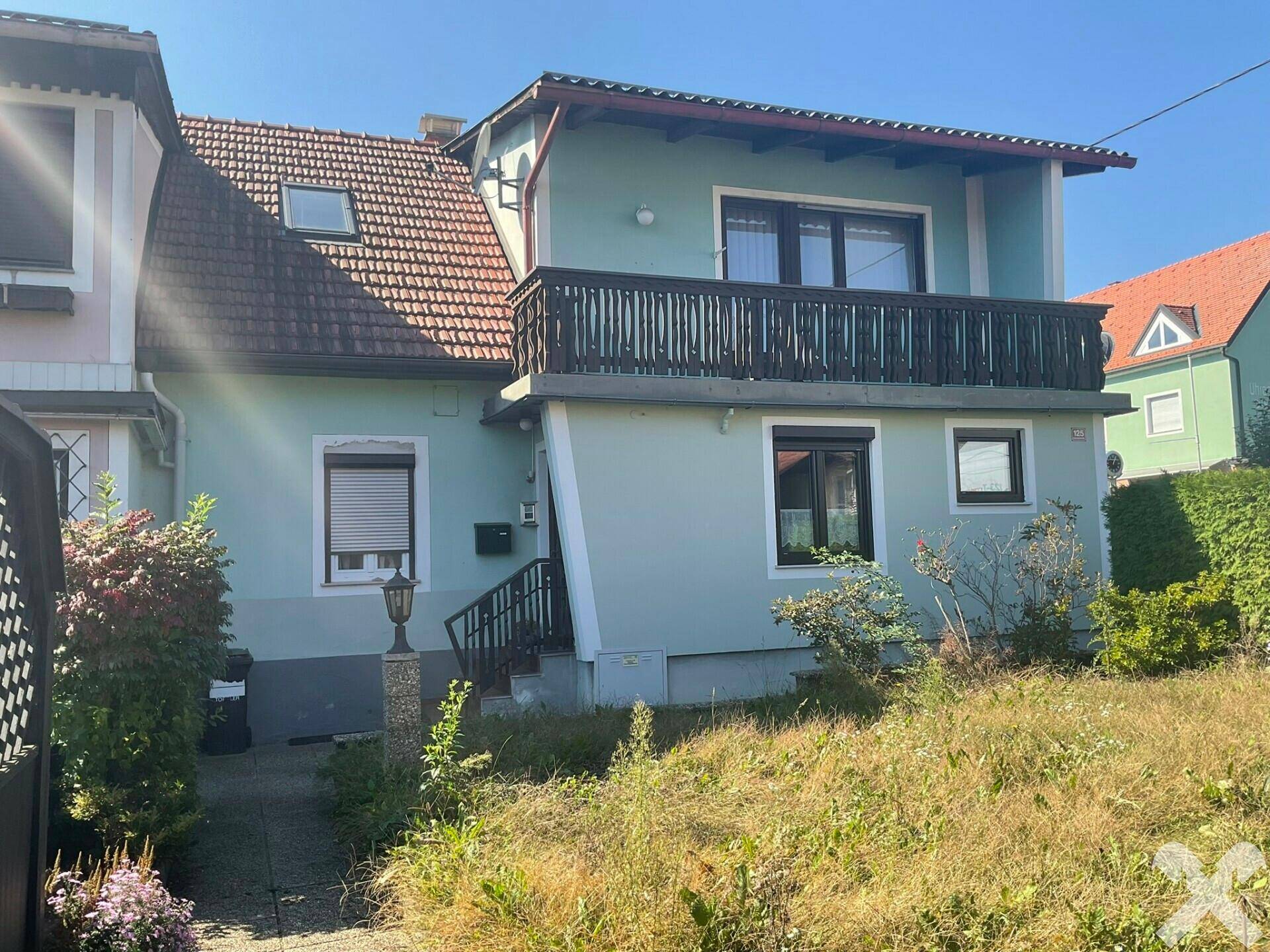 Vorderansicht des Hauses mit Balkon, Gartenbereich und Zugang zum Eingang.