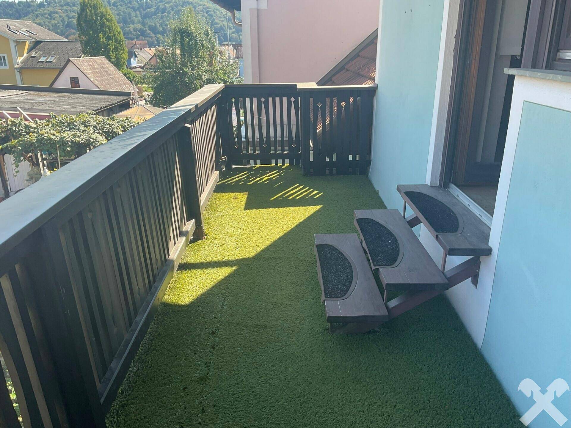 Balkon mit Kunstrasen, Holzgeländer und Blick auf die Umgebung.