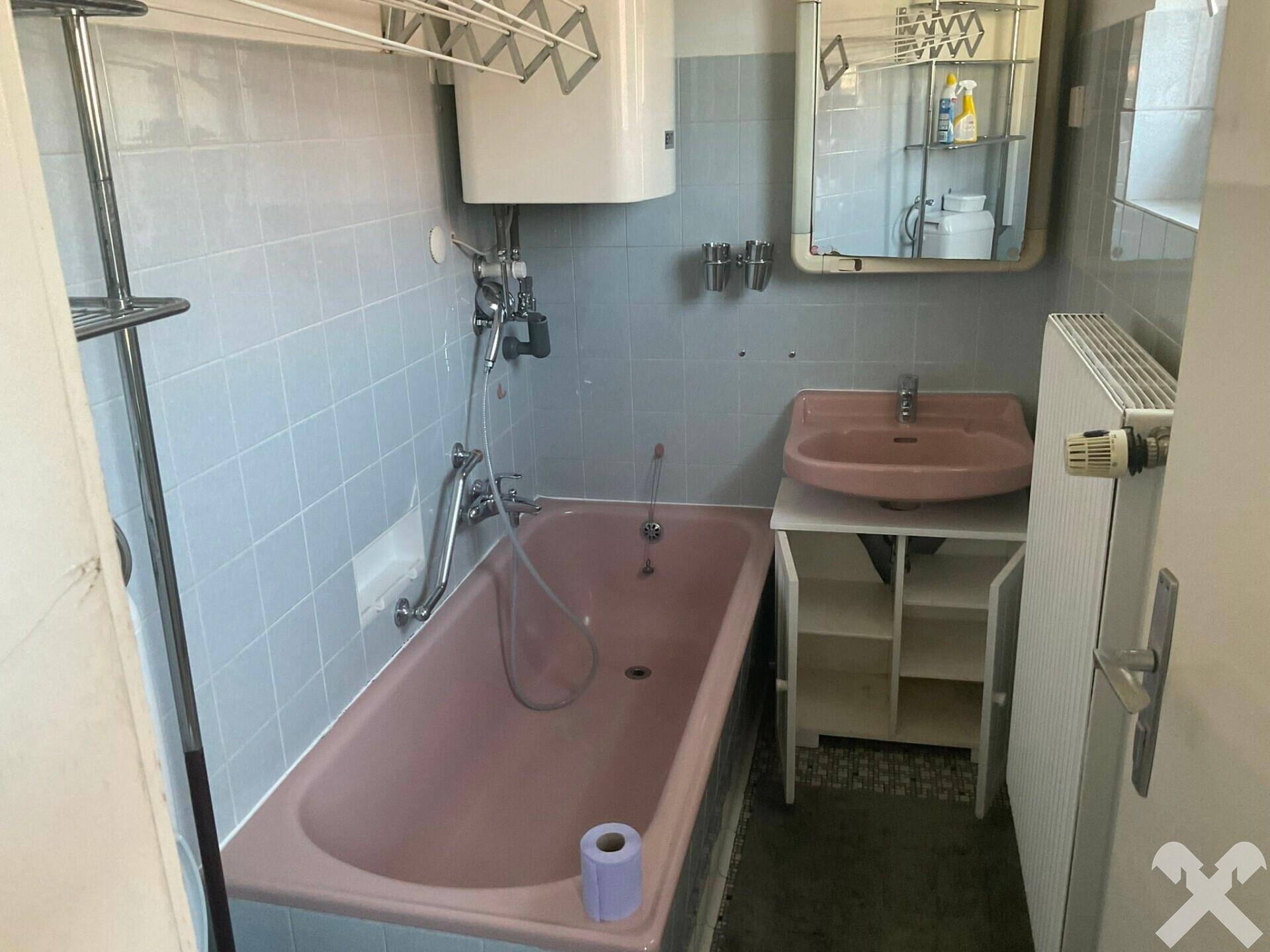 Badezimmer mit rosa Badewanne, Waschbecken und hellblauen Fliesen.