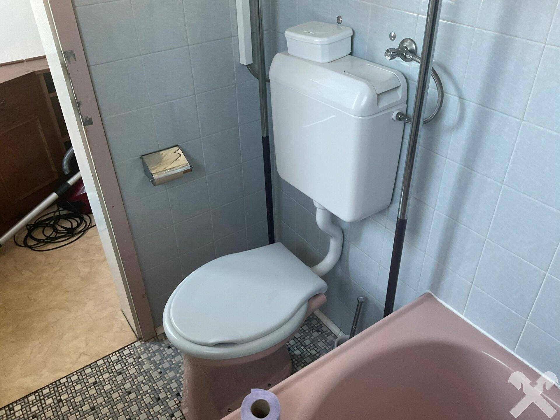 Toilette im Badezimmer mit hellblauen Fliesen und rosa Akzenten.