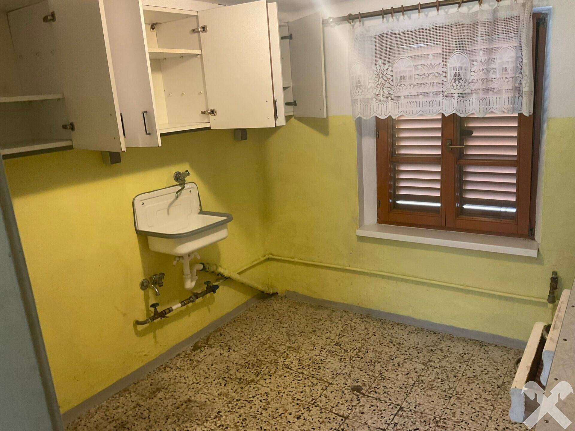 Einfacher Waschraum mit Spülbecken, gelben Wänden und Fenster mit Holzläden.
