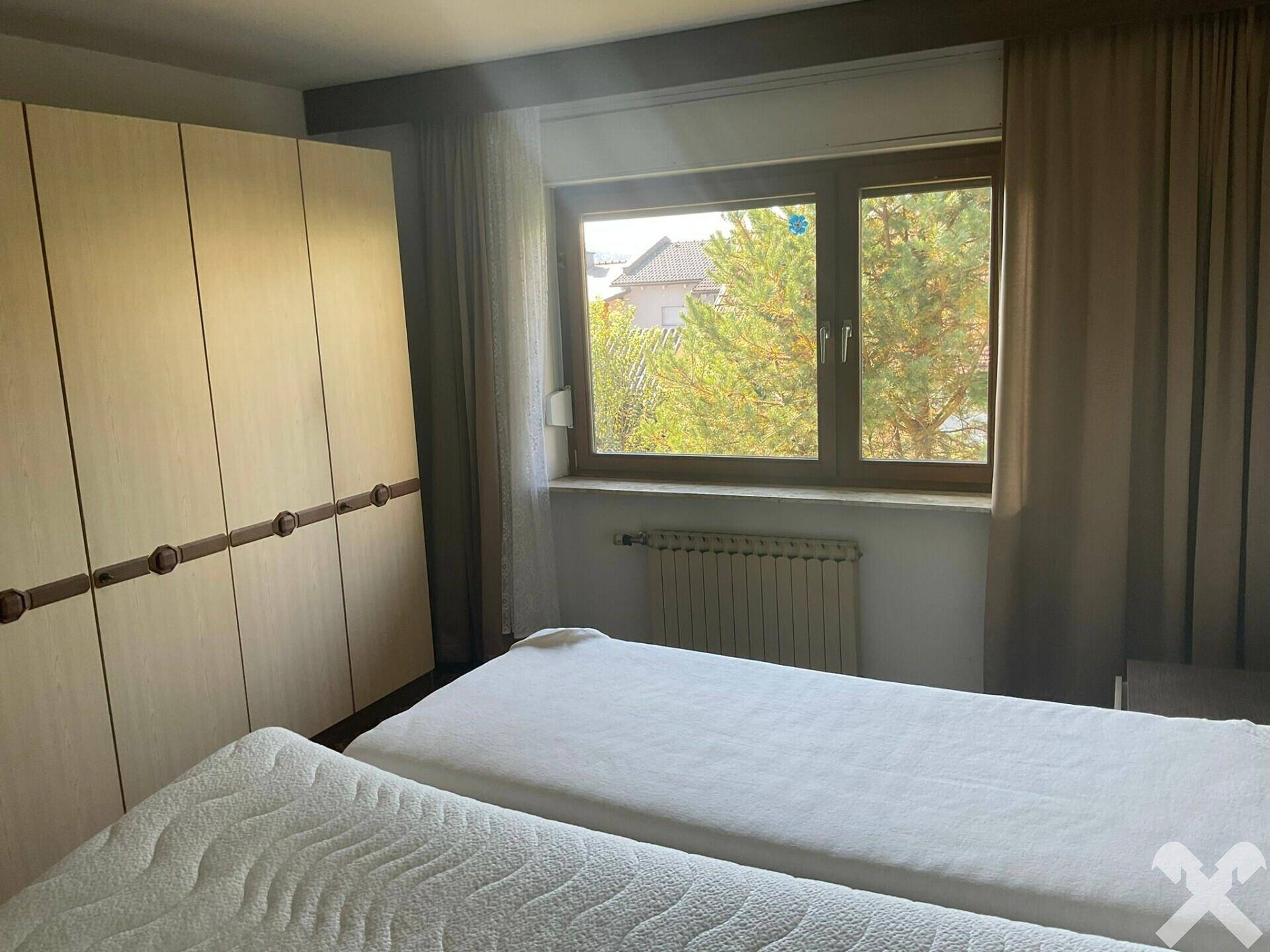 Schlafzimmer mit zwei Einzelbetten, großem Kleiderschrank und Fensterblick ins Grüne.