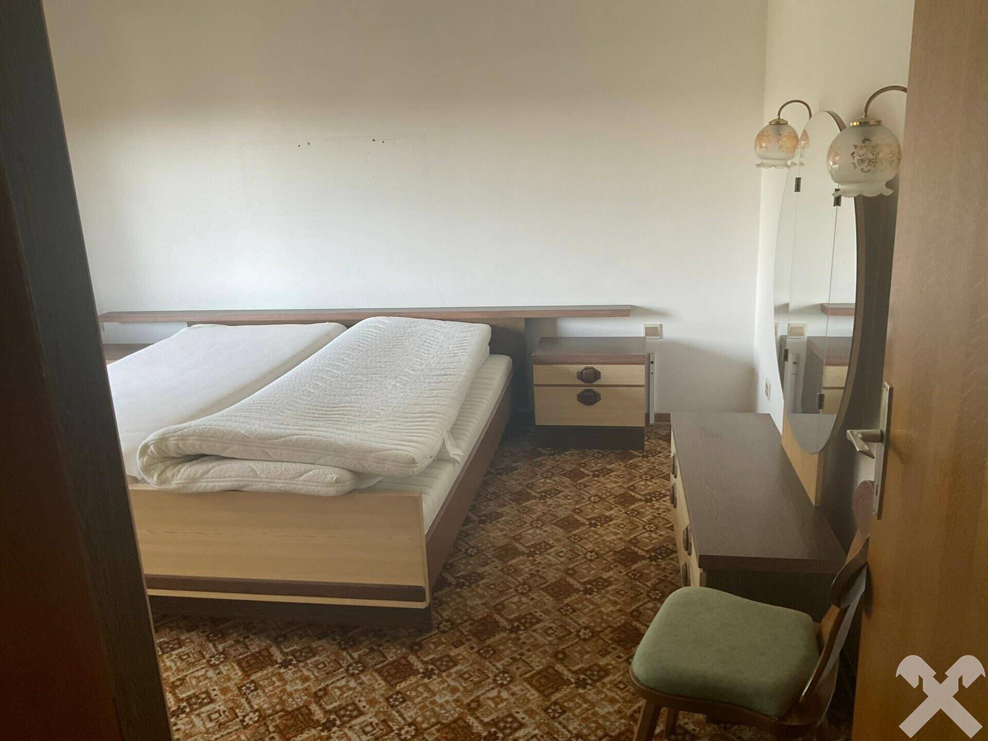 Schlafzimmer mit Doppelbett, Nachttischen und gemustertem Teppichboden.