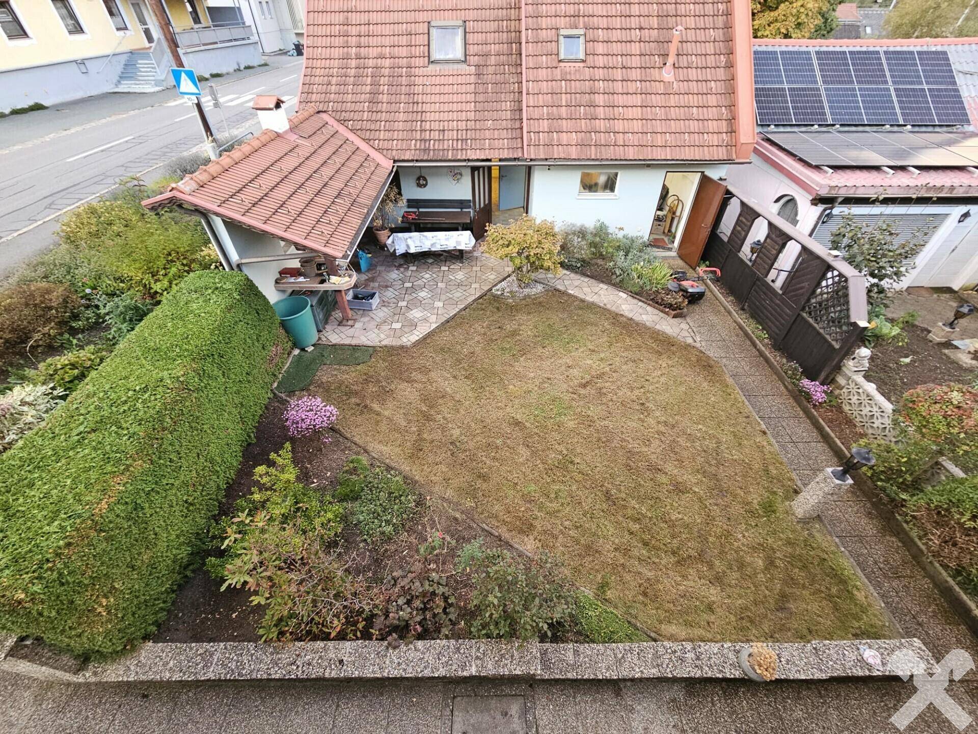 Gartenbereich mit Rasenfläche, gepflasterter Terrasse und Hecken.