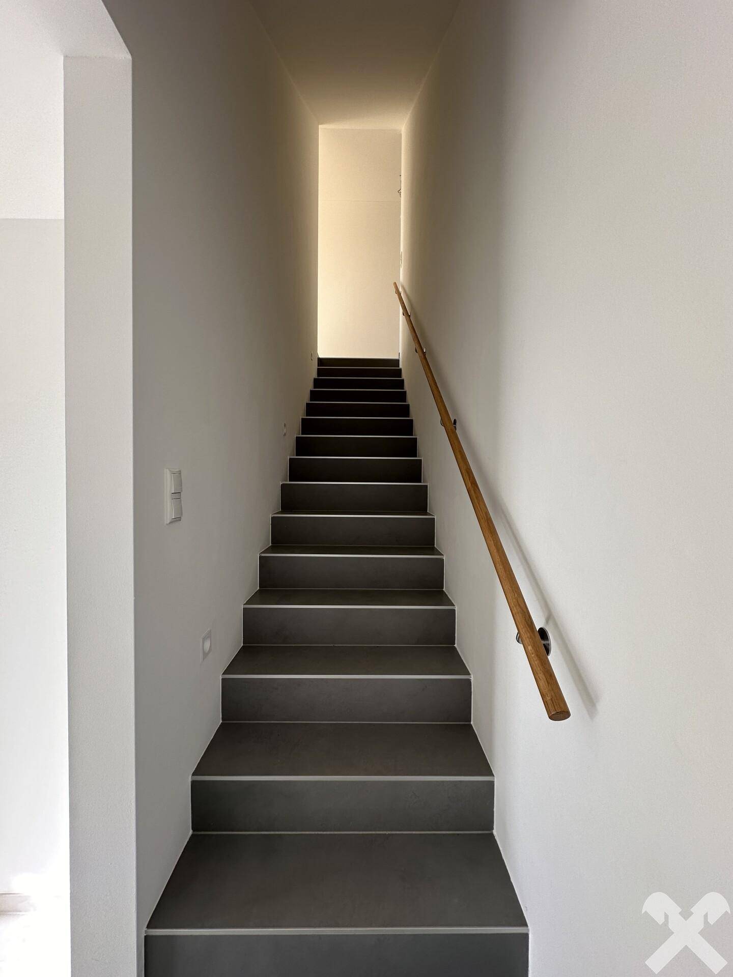 Helles Treppenhaus mit modernen grauen Fliesenstufen und einem eleganten Holzhandlauf, der nach oben führt.