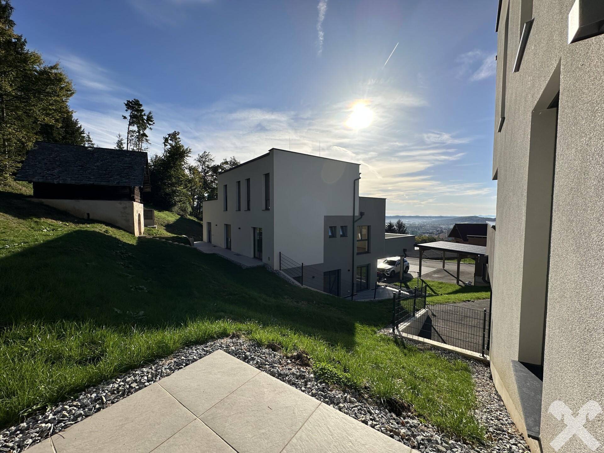 Moderne Wohngebäude auf einem grünen Hügel mit sonnigem Ausblick und umgebender Naturlandschaft.