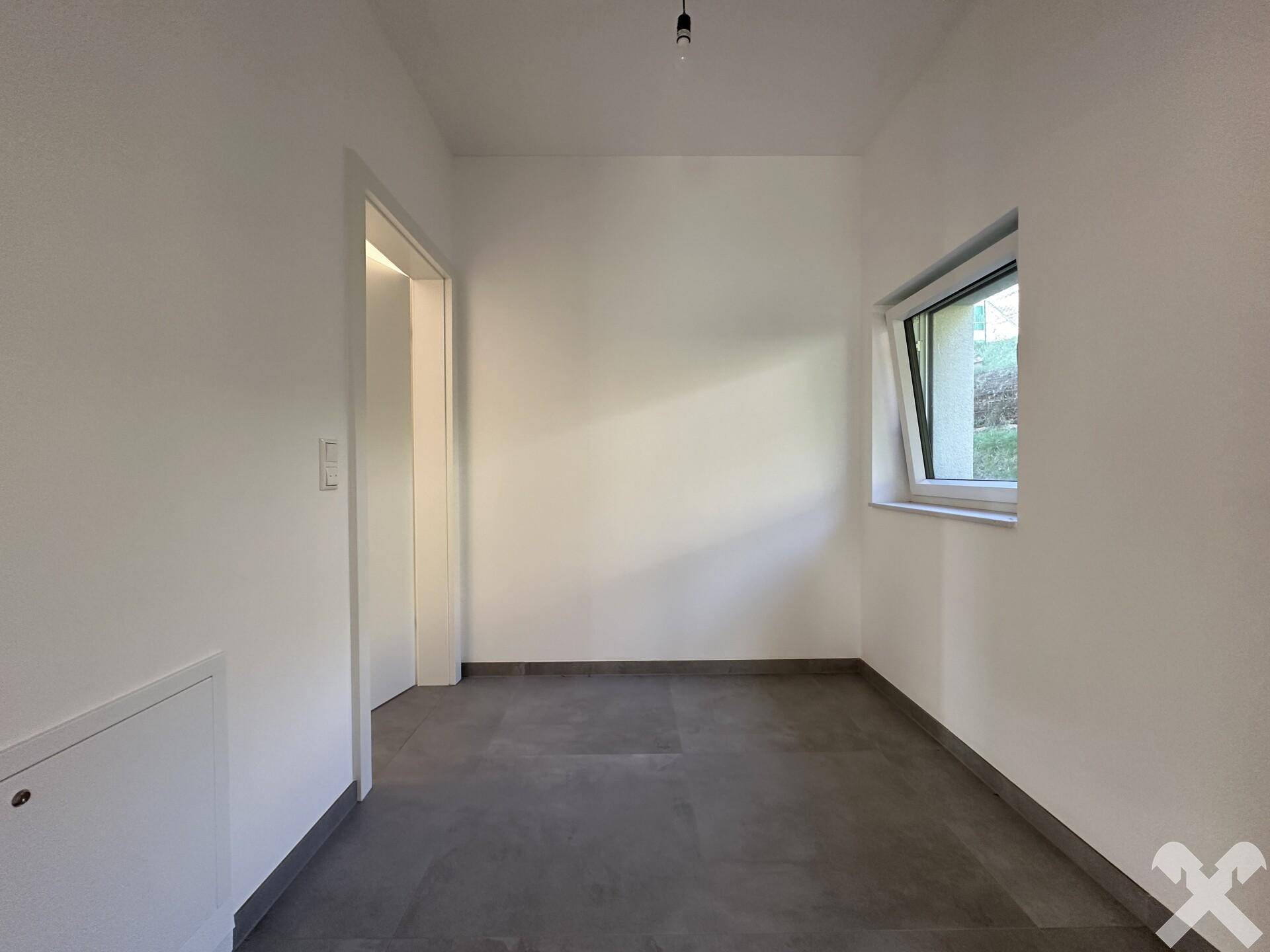 Kleiner, heller Raum mit grauen Fliesen und Fenster, geeignet als Abstellraum oder kleines Büro.