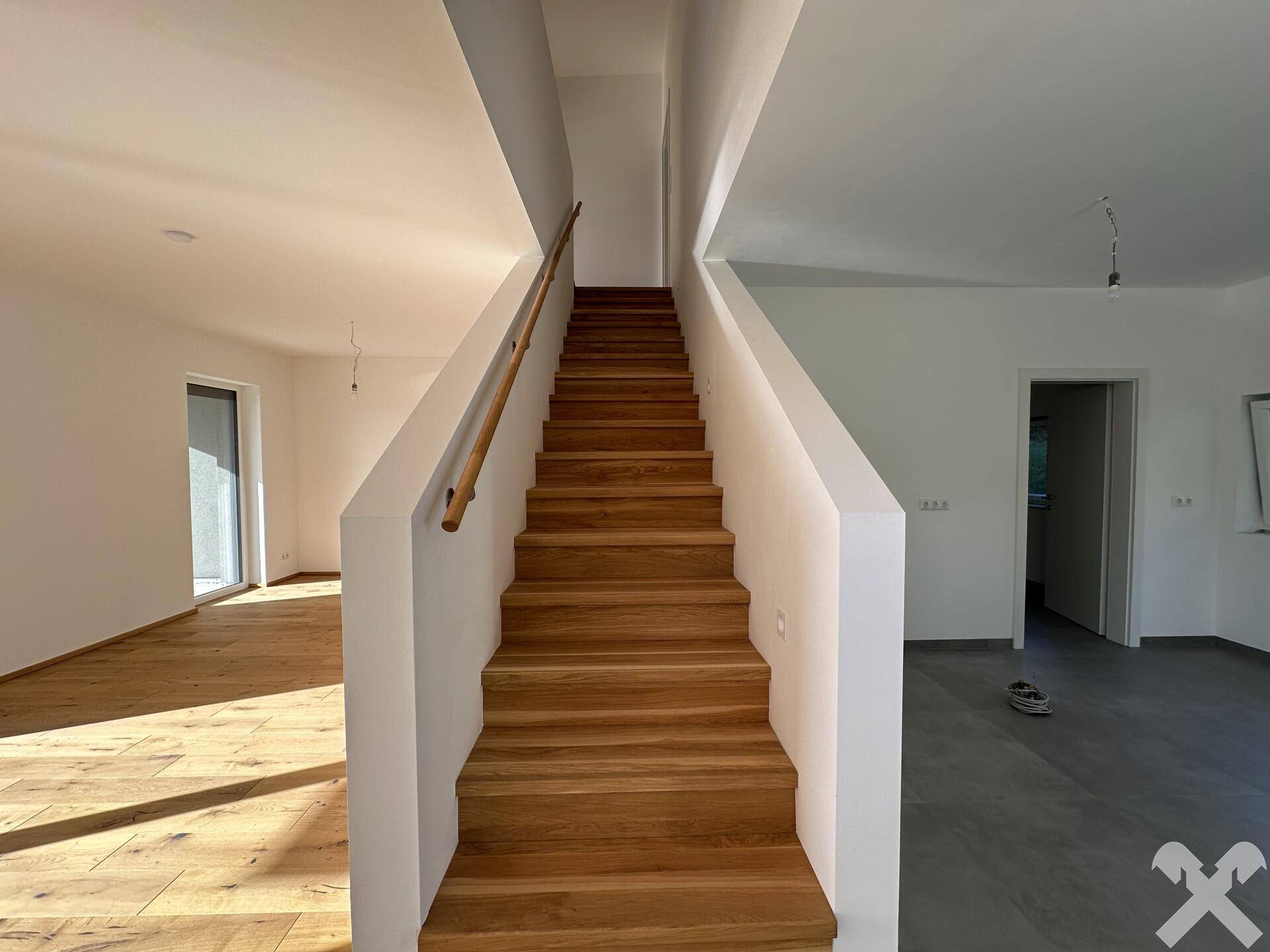 Lichtdurchflutetes Treppenhaus mit eleganten Holzstufen und weißem Geländer, das die verschiedenen Ebenen verbindet.