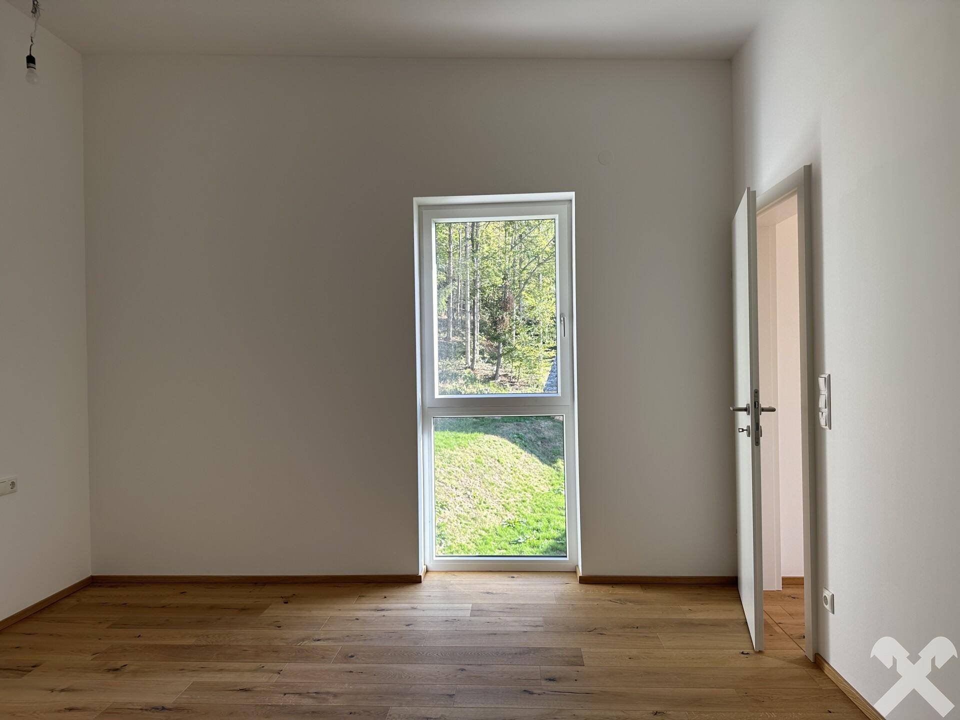 Helles Zimmer mit Eichenparkett und großem Fenster, das einen ruhigen Blick ins Grüne bietet.