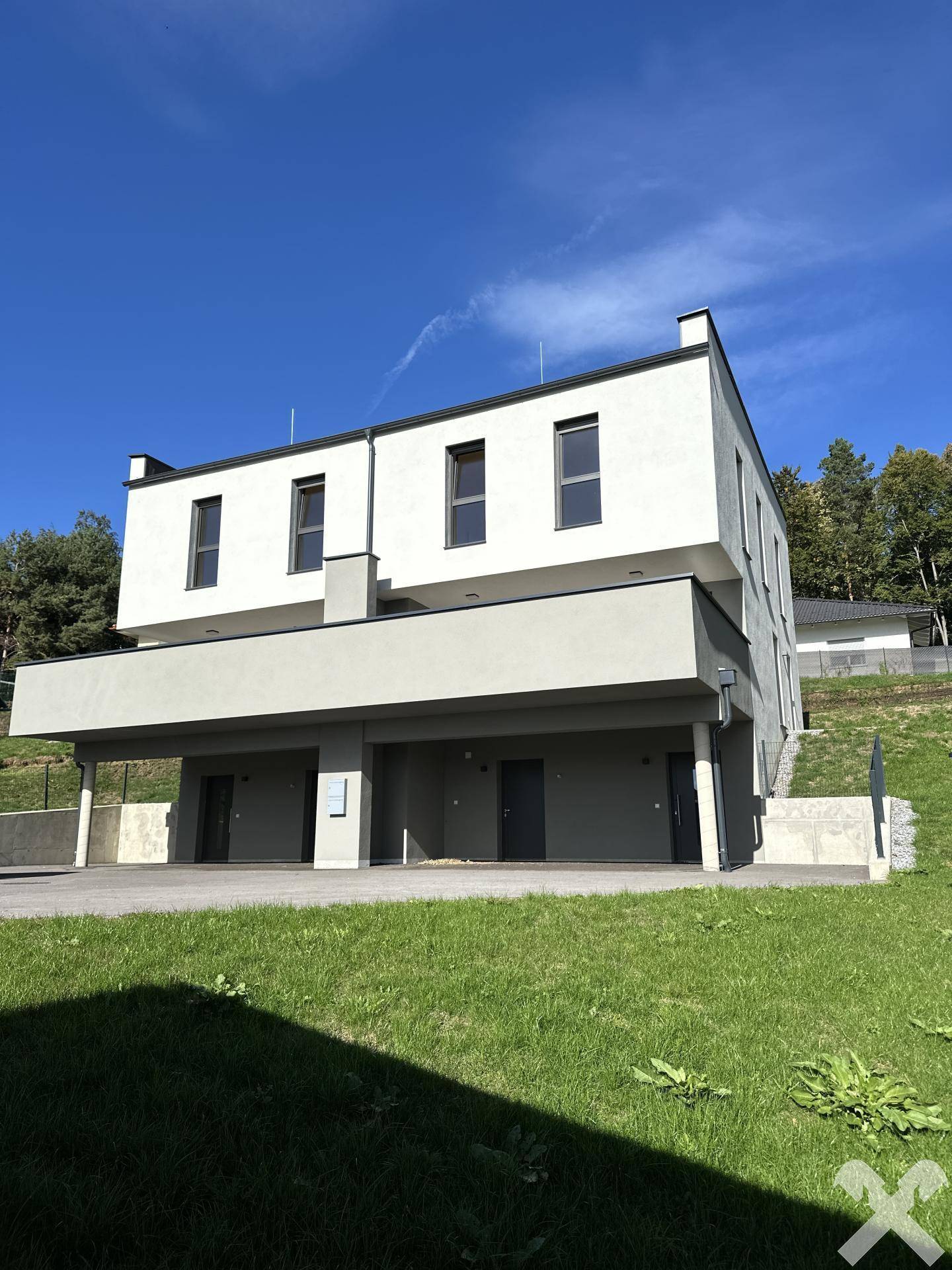 Moderne Architektur der Neubau-Doppelhaushälfte mit klaren Linien und großen Fenstern an einem sonnigen Hang.
