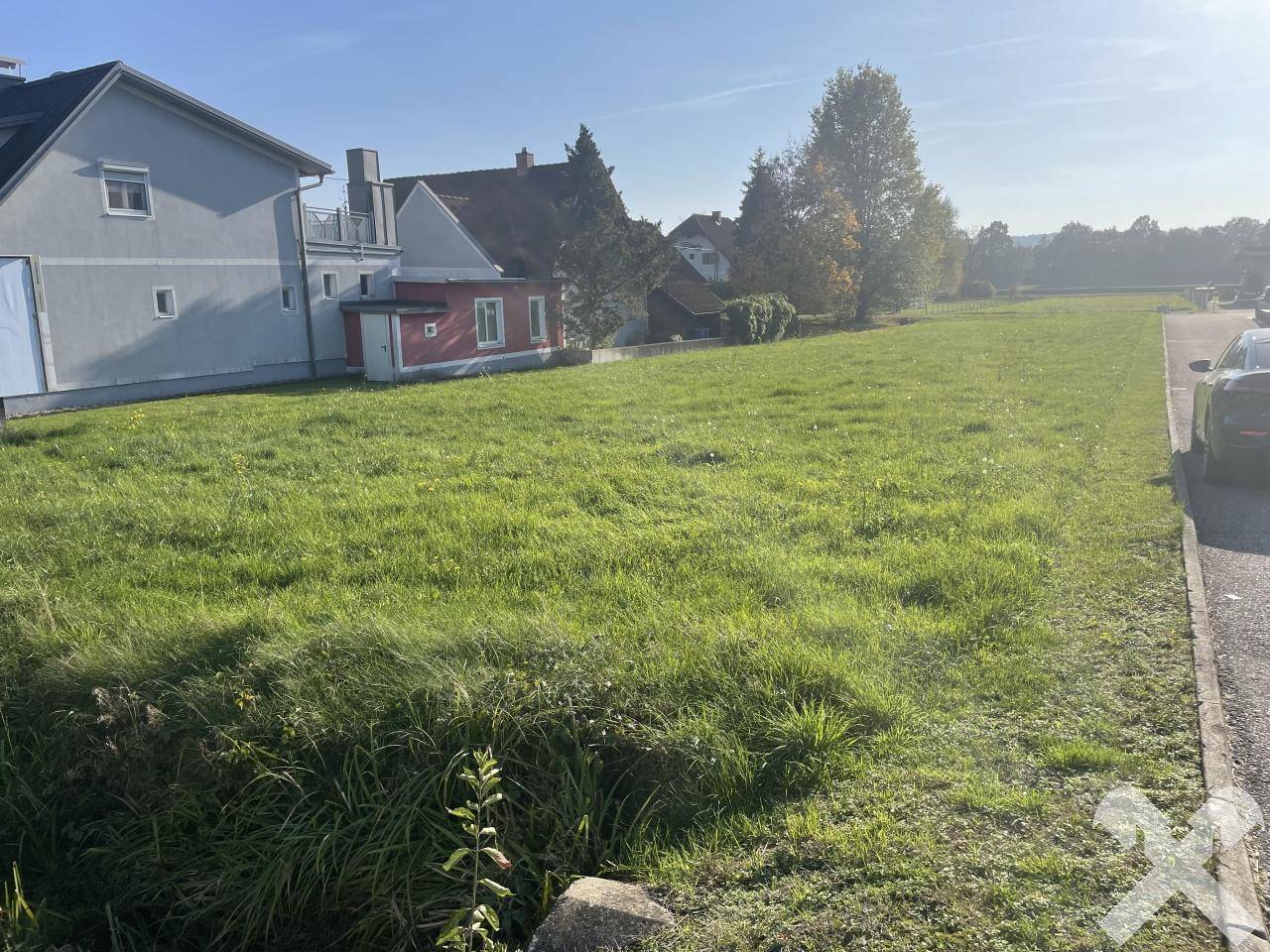 Weitläufiges grünes Grundstück mit angrenzenden Wohnhäusern und einer Straße unter blauem Himmel.