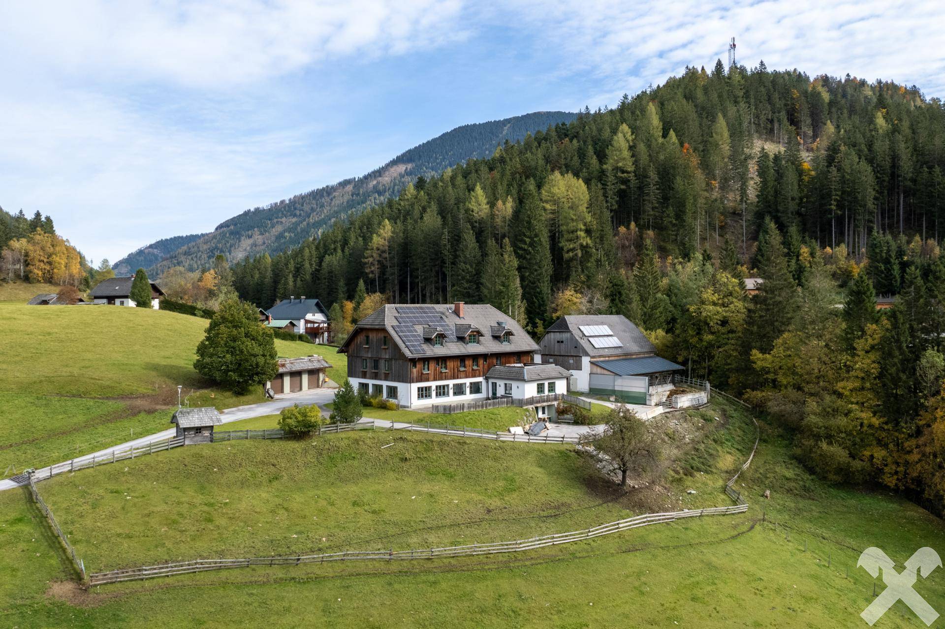 Malerisches Anwesen mit mehreren Gebäuden in einer weitläufigen Berglandschaft, umgeben von grünen Wiesen und Wäldern.