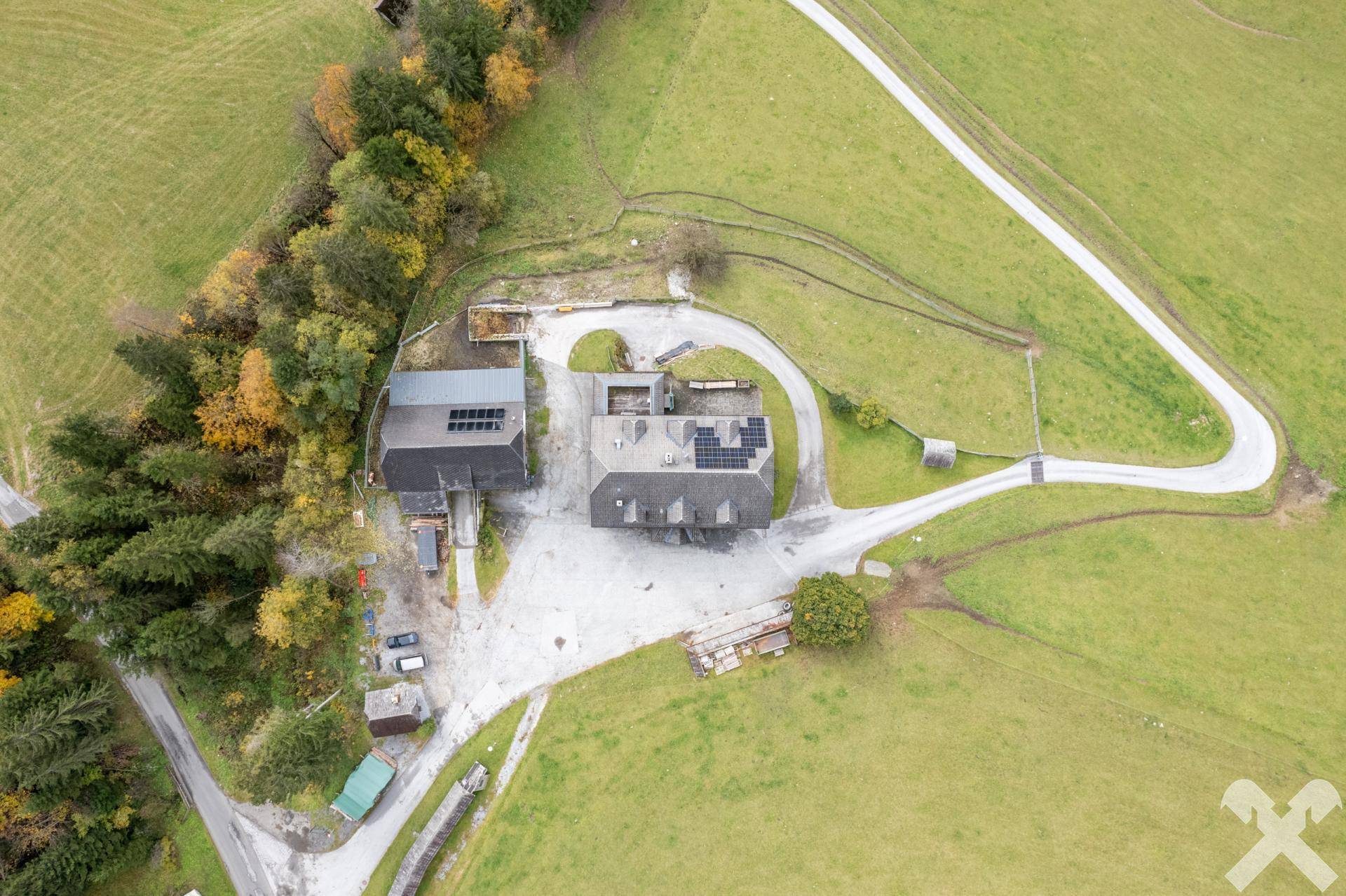 Luftaufnahme des gesamten Anwesens mit Gebäuden, Zufahrten und umliegenden Wiesen und Wäldern in einer Bergregion.