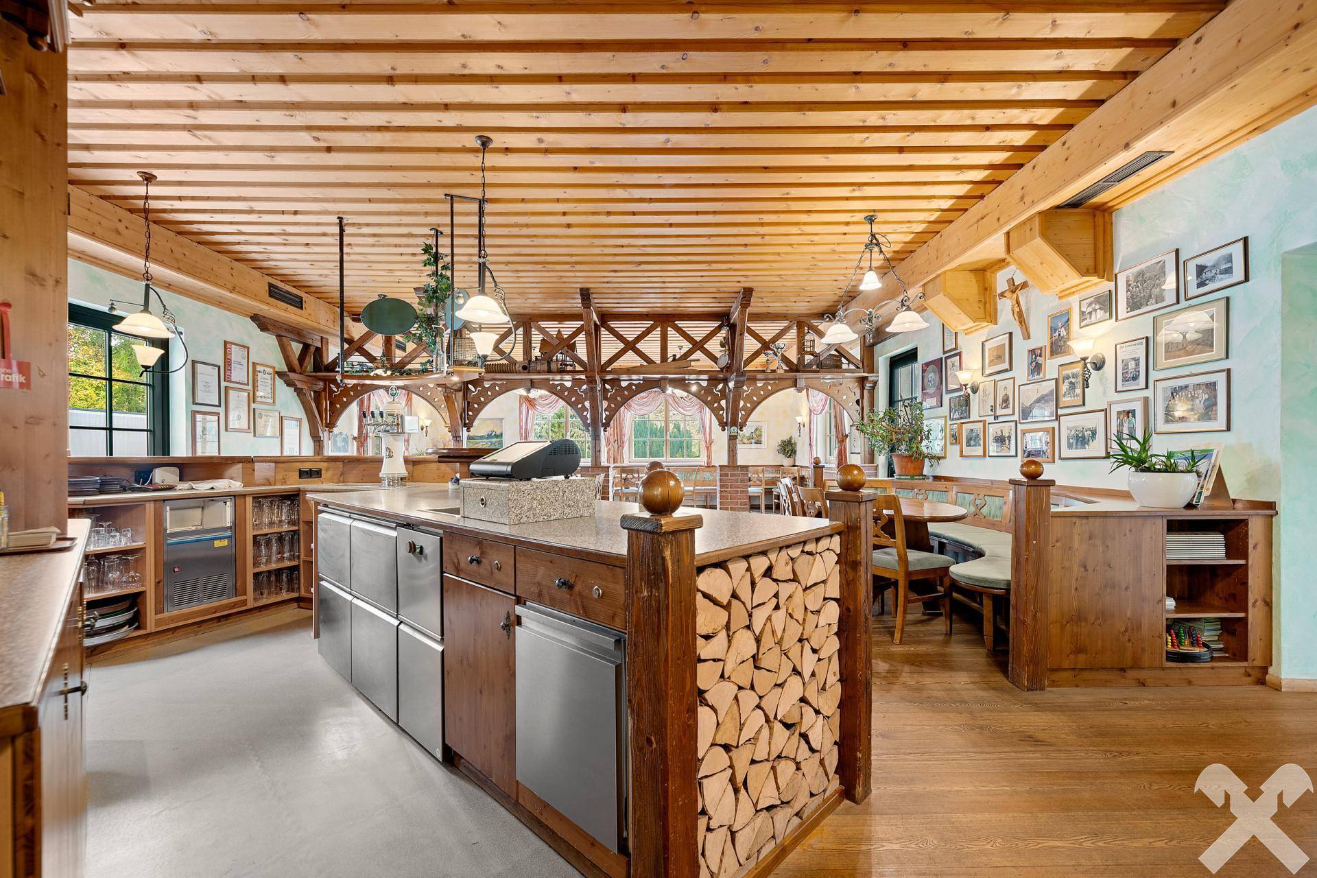 Rustikaler Thekenbereich mit Holzverkleidung, integrierten Geräten und einem dekorativen Holzstapel, funktional und stilvoll.