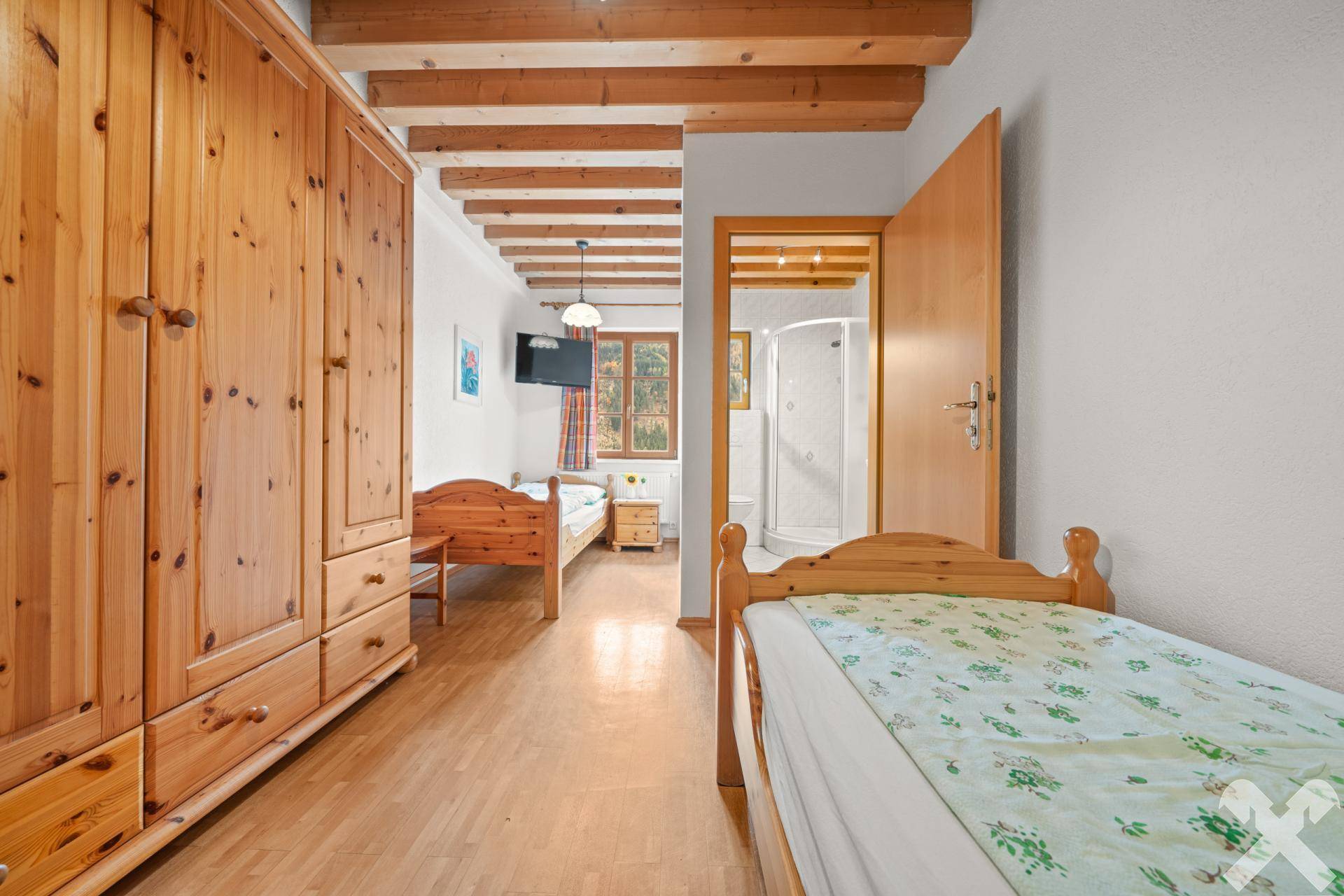 Einfaches Schlafzimmer mit Holzbalkendecke, Holzboden und zwei Einzelbetten, ideal für Gäste oder Kinder.