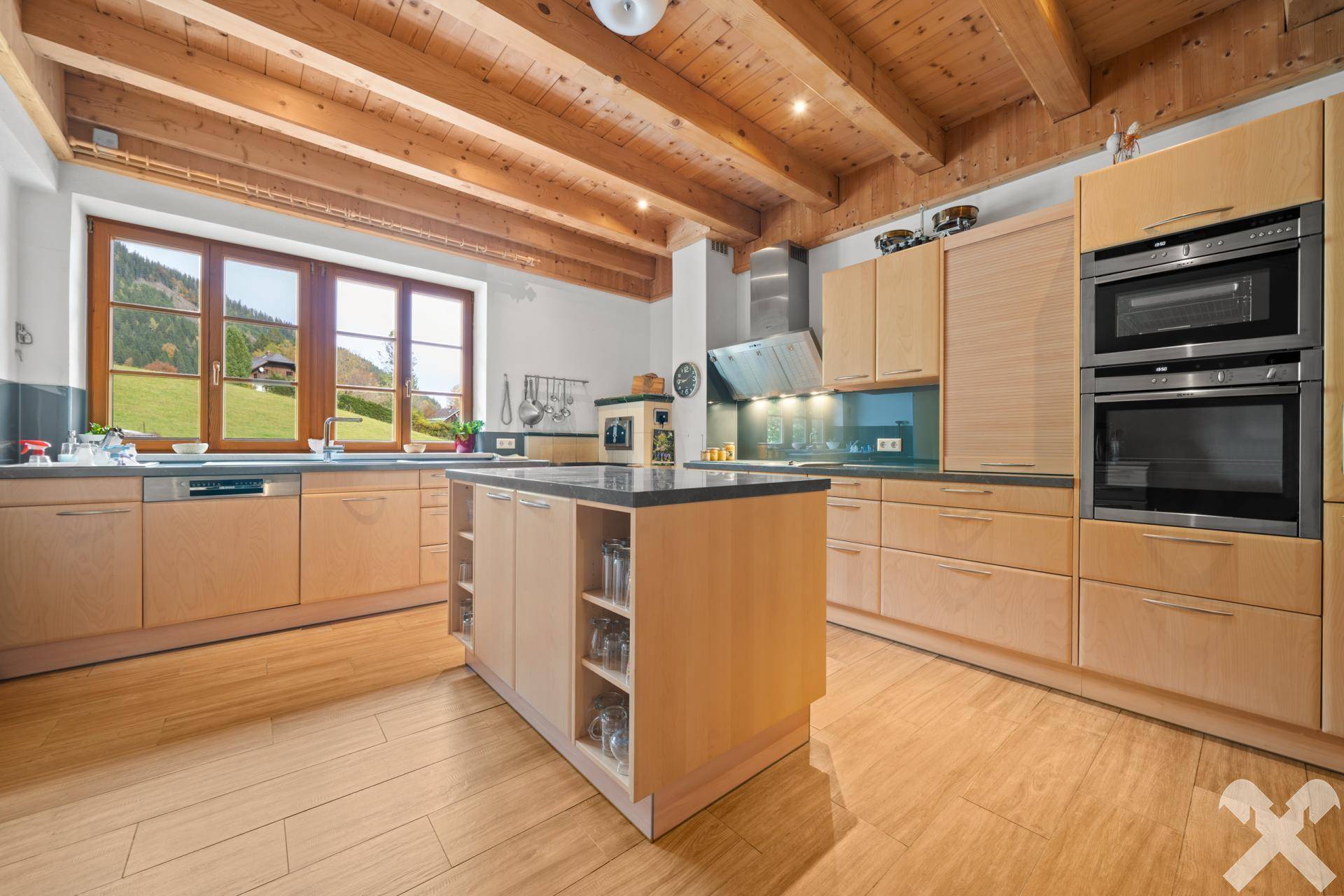 Helle, moderne Küche mit Holzschränken, Kochinsel, Einbaugeräten und Fenster mit Bergblick, funktional und stilvoll.