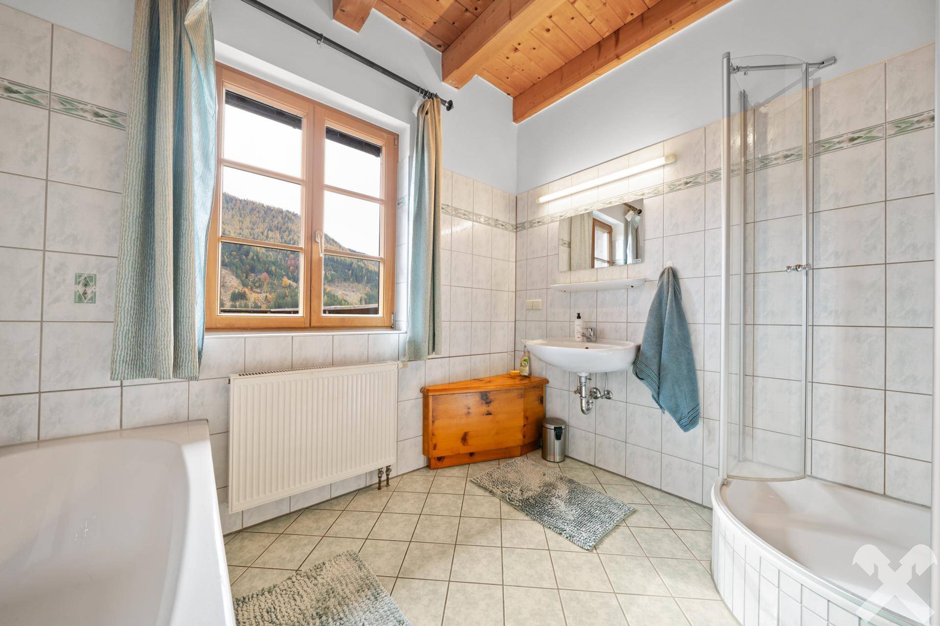 Helles Badezimmer mit Badewanne, Duschkabine, Waschtisch und Fenster mit Bergblick, bietet Komfort und Funktionalität.