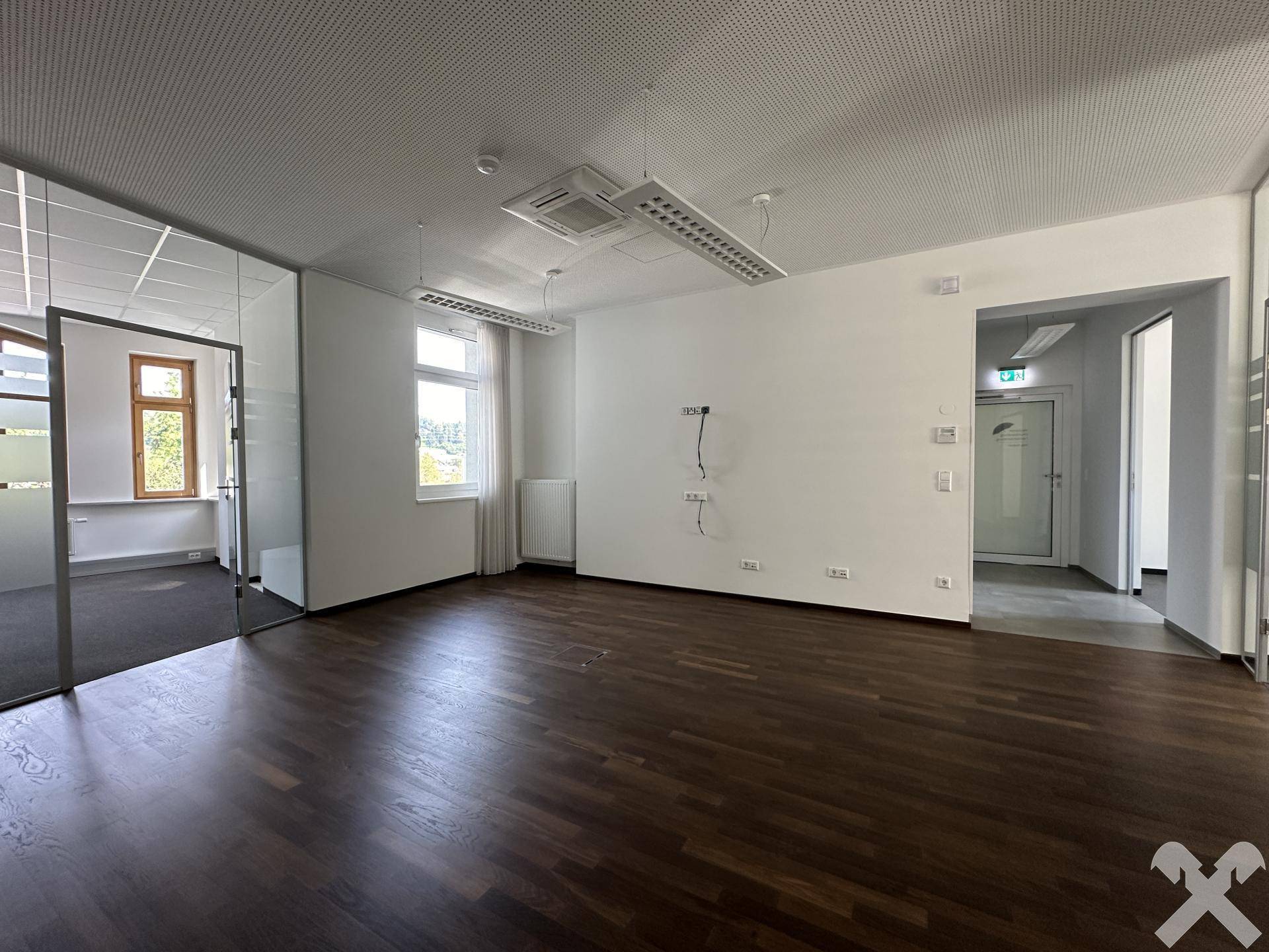 Helles Büro mit Holzboden, großen Fenstern und flexiblen Glaswänden, bereit für individuelle Gestaltung und Nutzung.