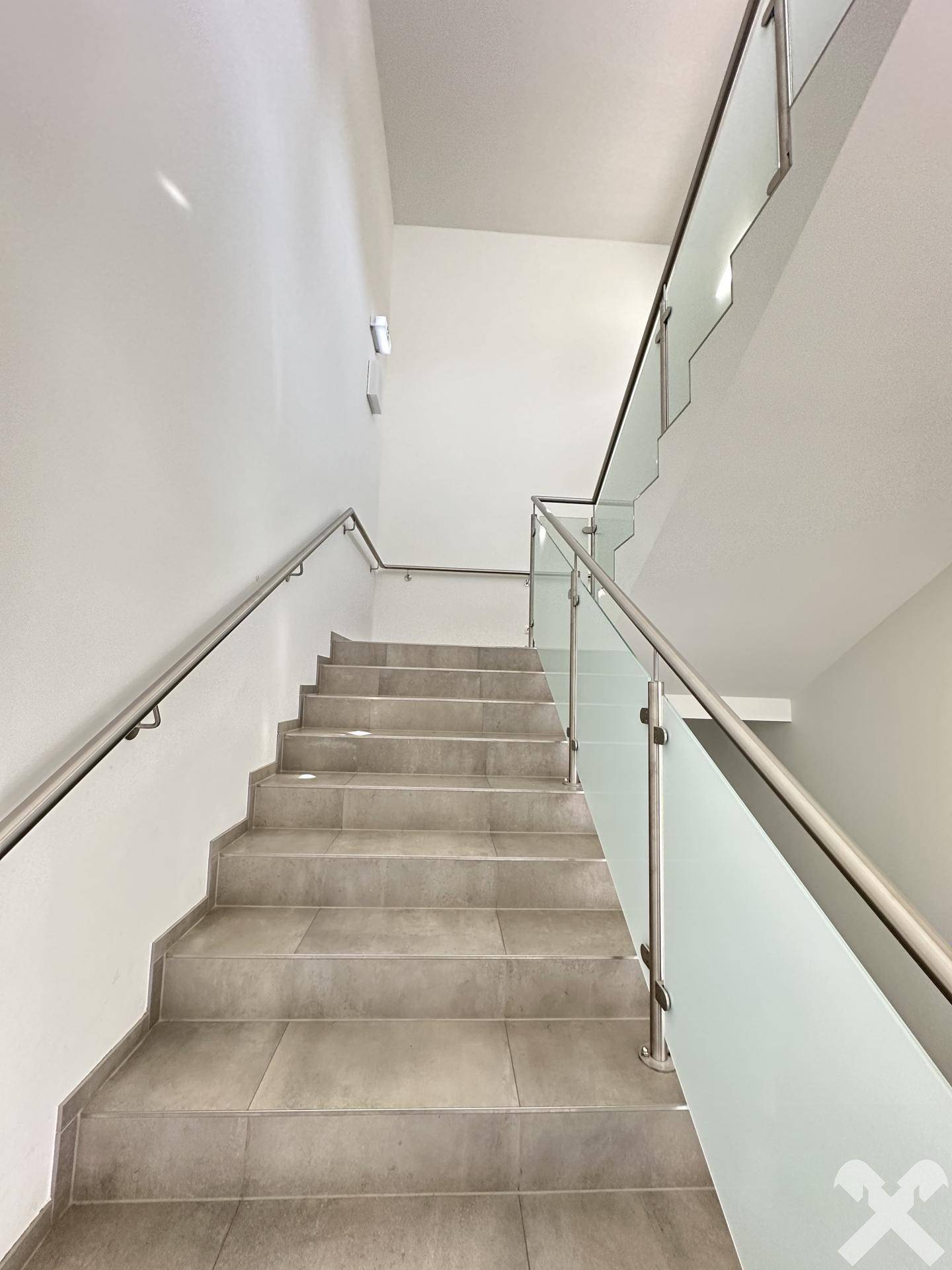 Helles Treppenhaus mit modernen Fliesenstufen, Edelstahlgeländer und Glasbrüstung, verbindet die Etagen elegant.